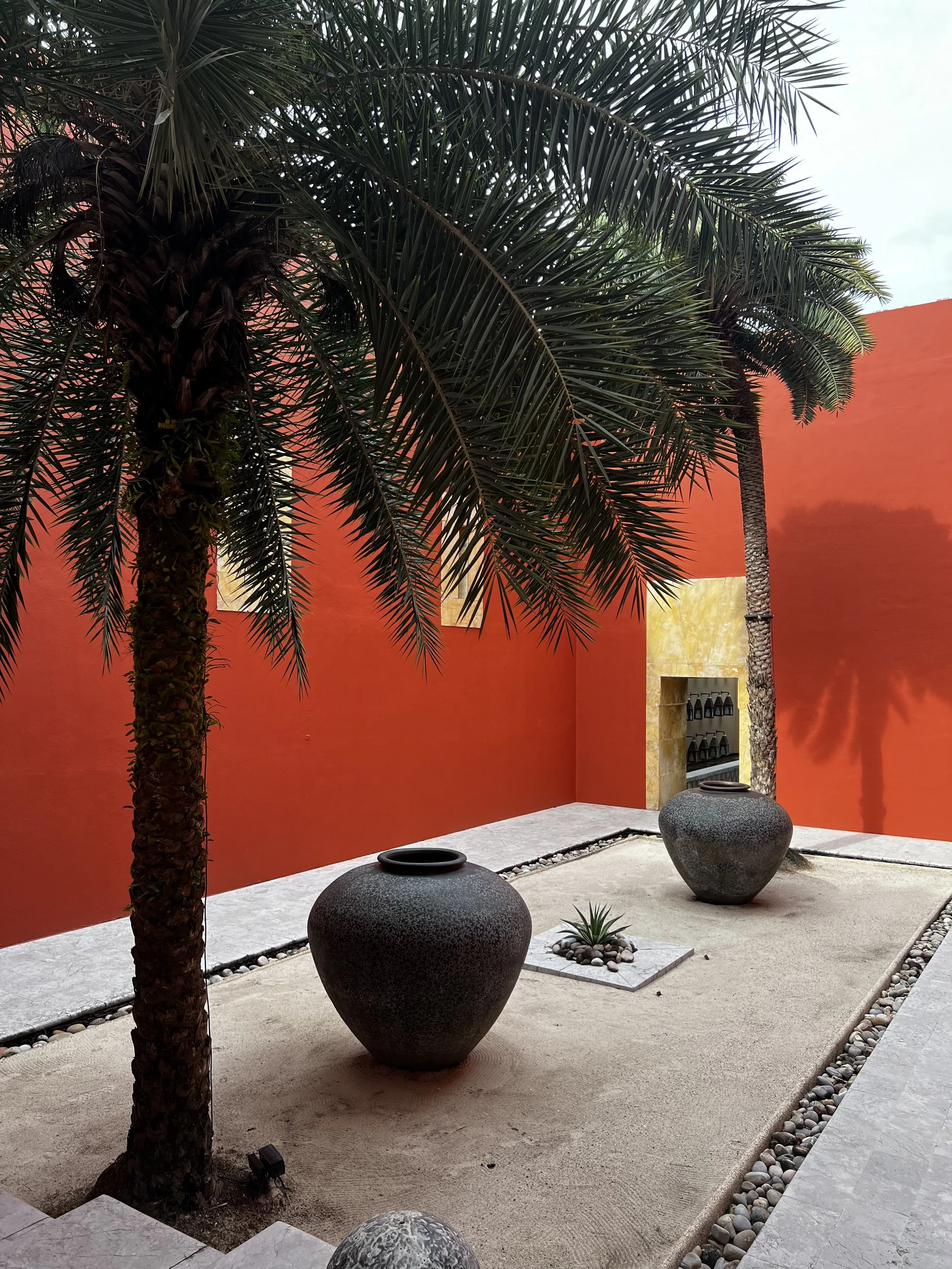 Modernist hotel courtyard with bold red walls, palm trees and dark ceramic vessels, Langkawi — ALTEZA Journal