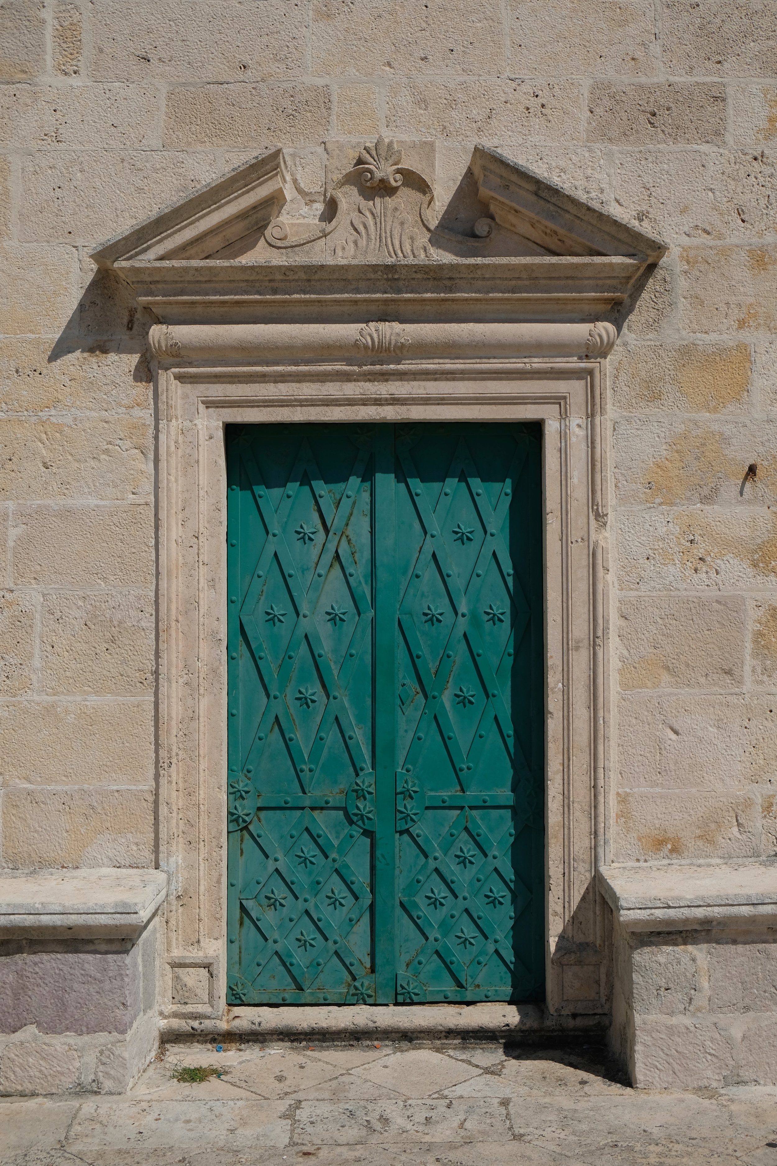 Ornate carved stone doorway with teal painted wooden doors and classical pediment detail — ALTEZA considered travel design