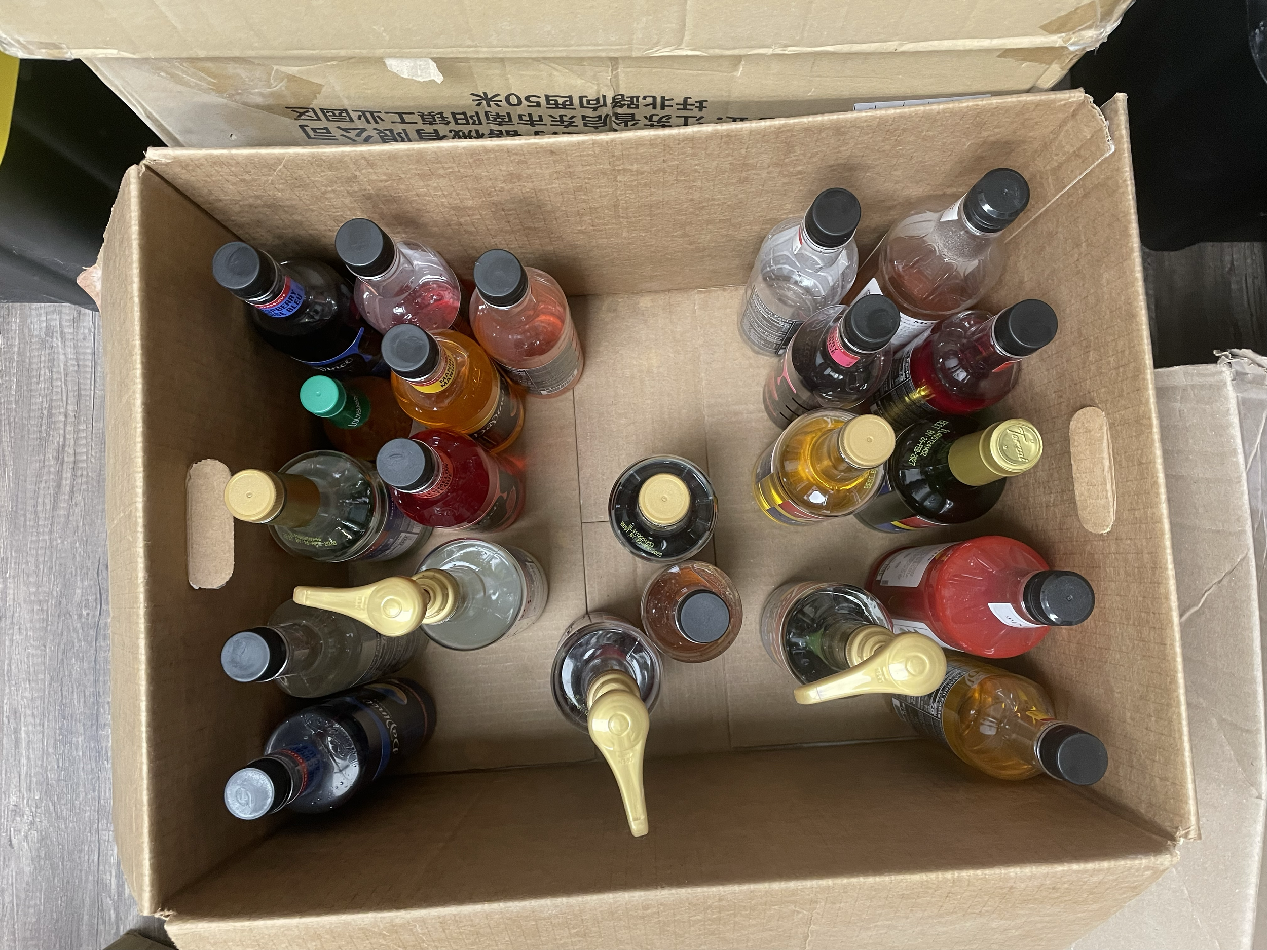 Box filled with various bottles of condiments and sauces, including soy sauce, hot sauce, and vinegar, viewed from above.