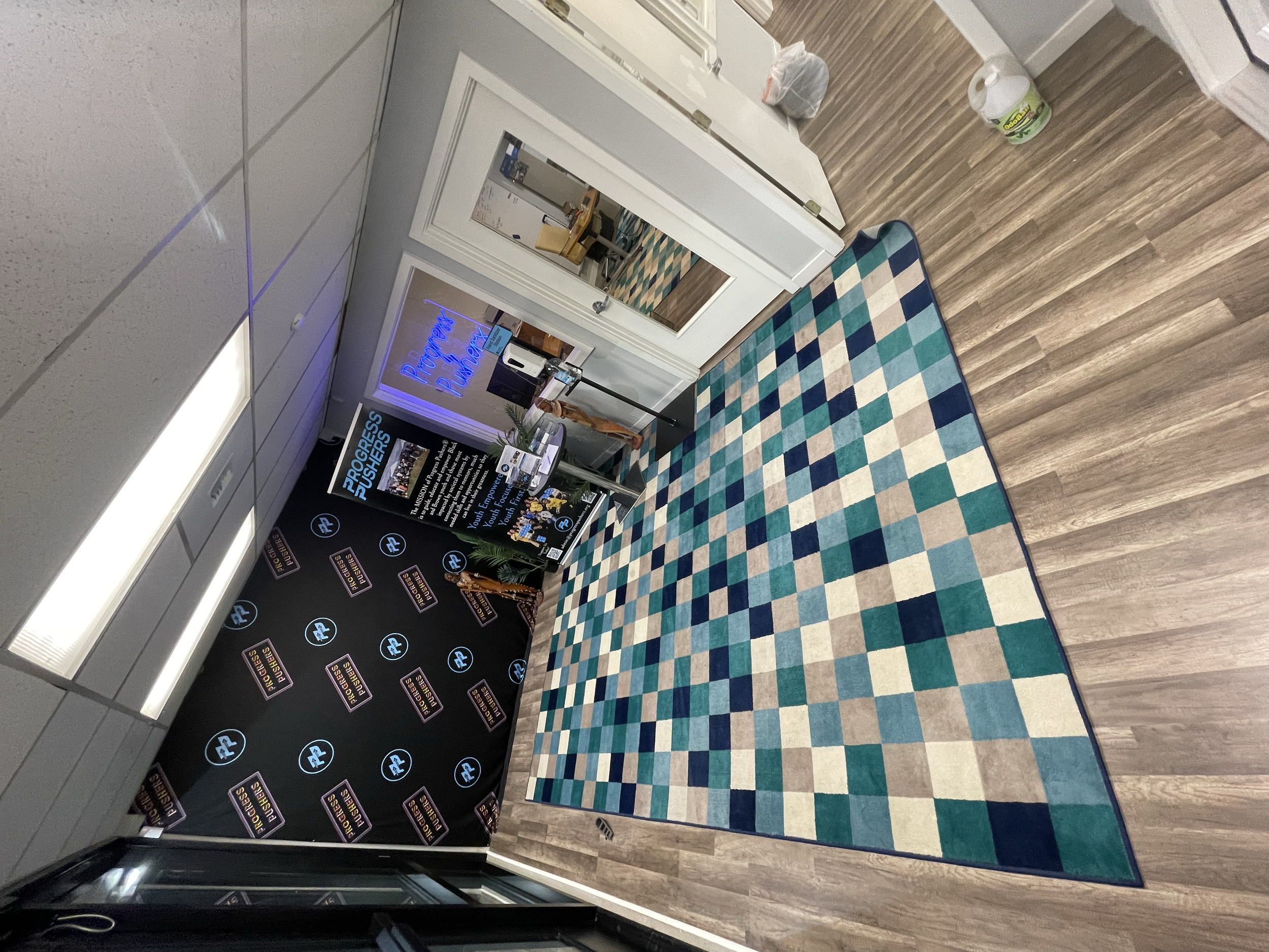 Interior of a conference or event space with a colorful checkered rug, promotional banners and digital signage for 'Progress Pioneers', and a large mirror on the wall.
