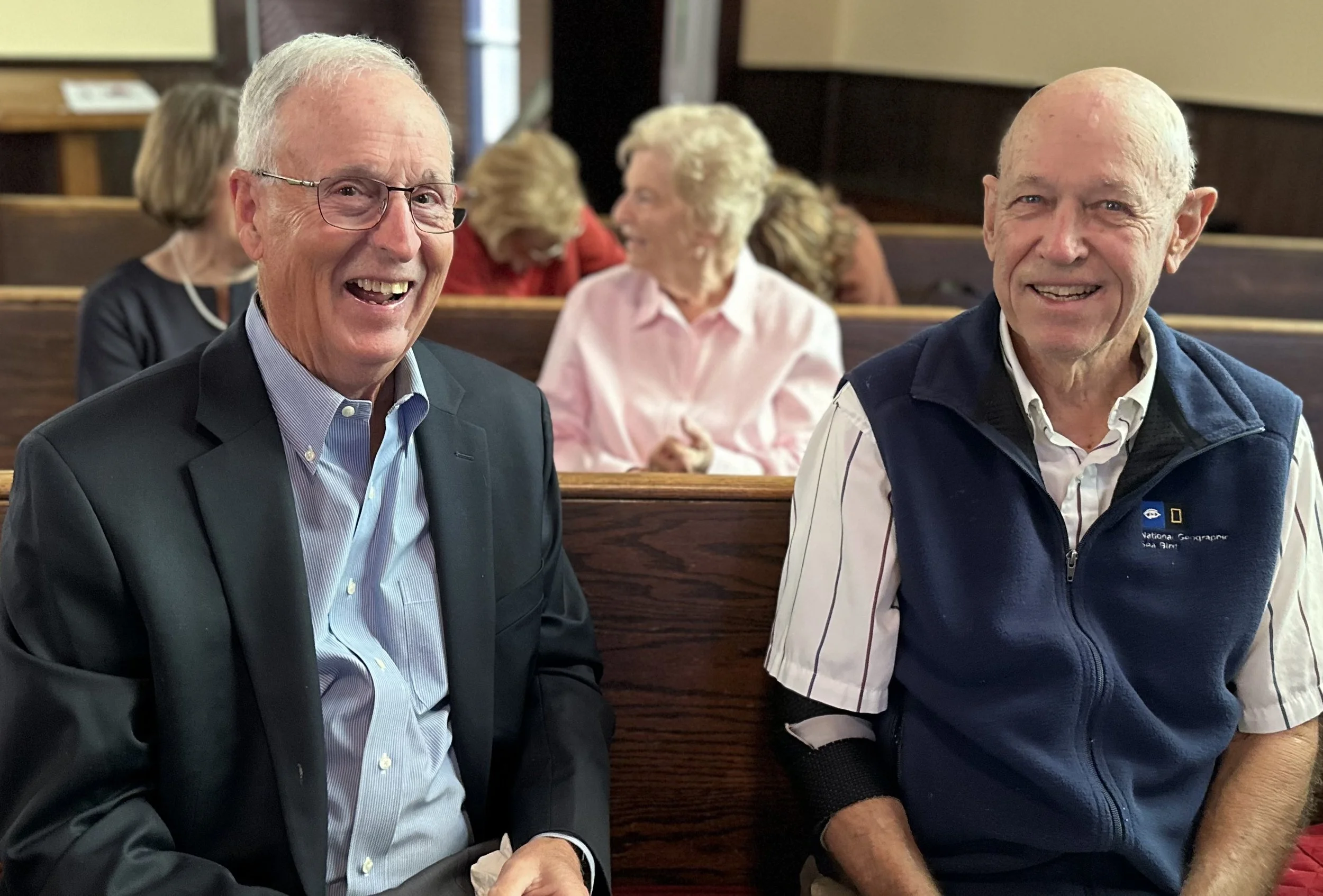 two men seated in a church pew smiling 