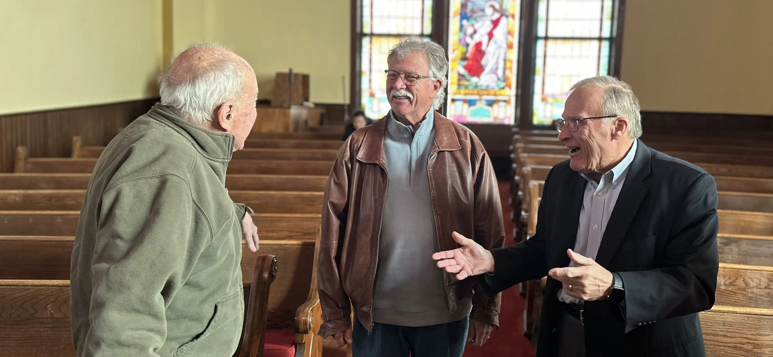 three men having a conversation while standing in the church sanctuary