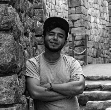 Arquitecto Robinson Pinzón. Joven posando con brazos cruzados junto a una pared de piedras en un lugar exterior.