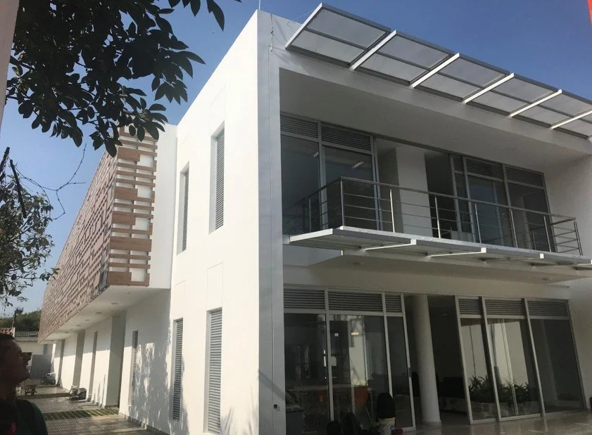Vista exterior de la Estación de Policía Cero Energía en Florida, Valle, Colombia, de dos pisos con estructura blanca y detalles metálicos, ventanas grandes con persianas, balcón con barandal de metal y paneles solares en el techo