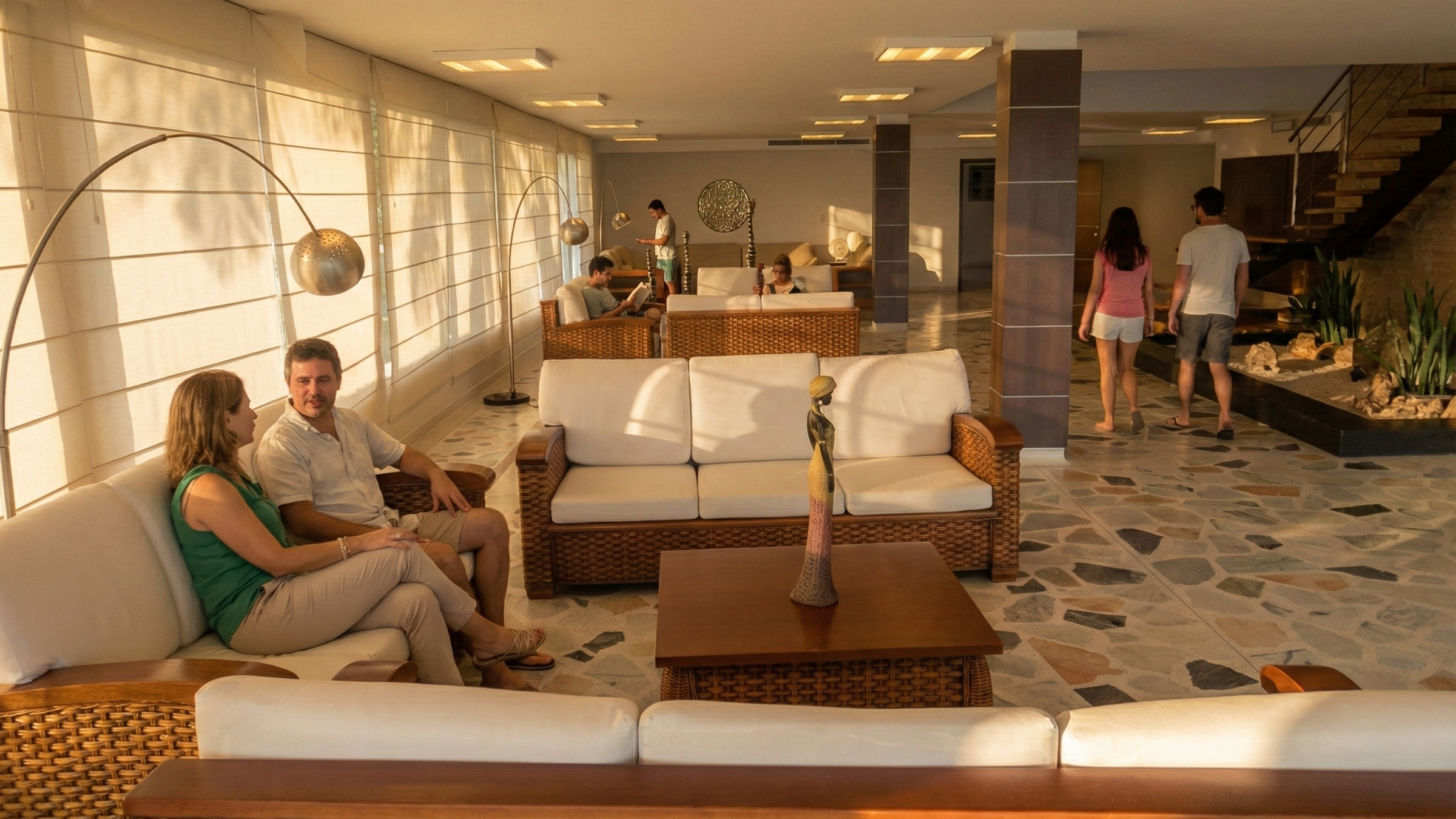 Vestíbulo de hotel con varias personas sentadas y paseando, decorado con muebles de madera, vegetación y decoraciones modernas.