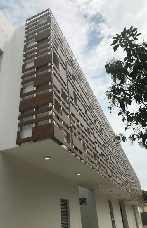 Estrategia de protección solar en la Estación de Policía Cero Energía en Florida, Valle, Colombia. Edificio moderno con fachada de madera y ventanas alineadas, bajo un cielo parcialmente nublado.
