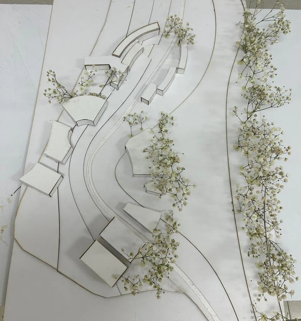 Maqueta de un diseño arquitectónico con caminos, áreas verdes con flores y estructuras de edificios o viviendas blanco y negros.