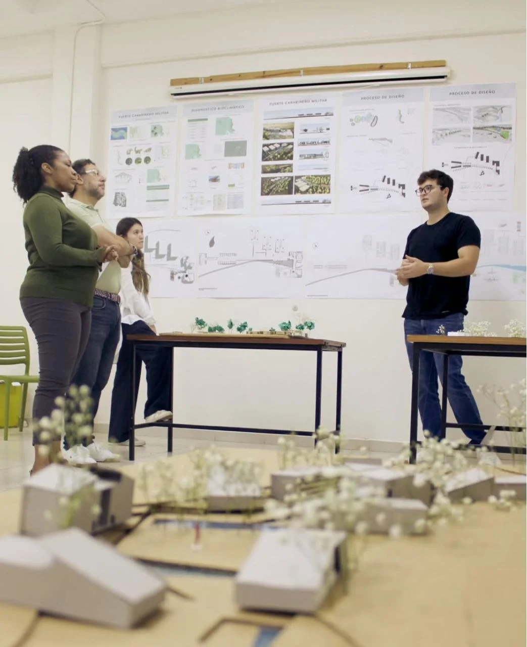 Estudiantes en una presentación de proyecto de diseño en un aula con planos y maquetas en la pared y en la mesa en la Escuela de Arquitectura y Diseño Isthmus en Panamá.