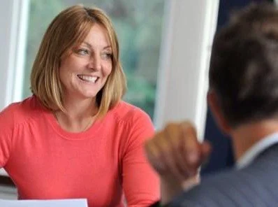 A woman smiling and speaking with a man in a professional setting.