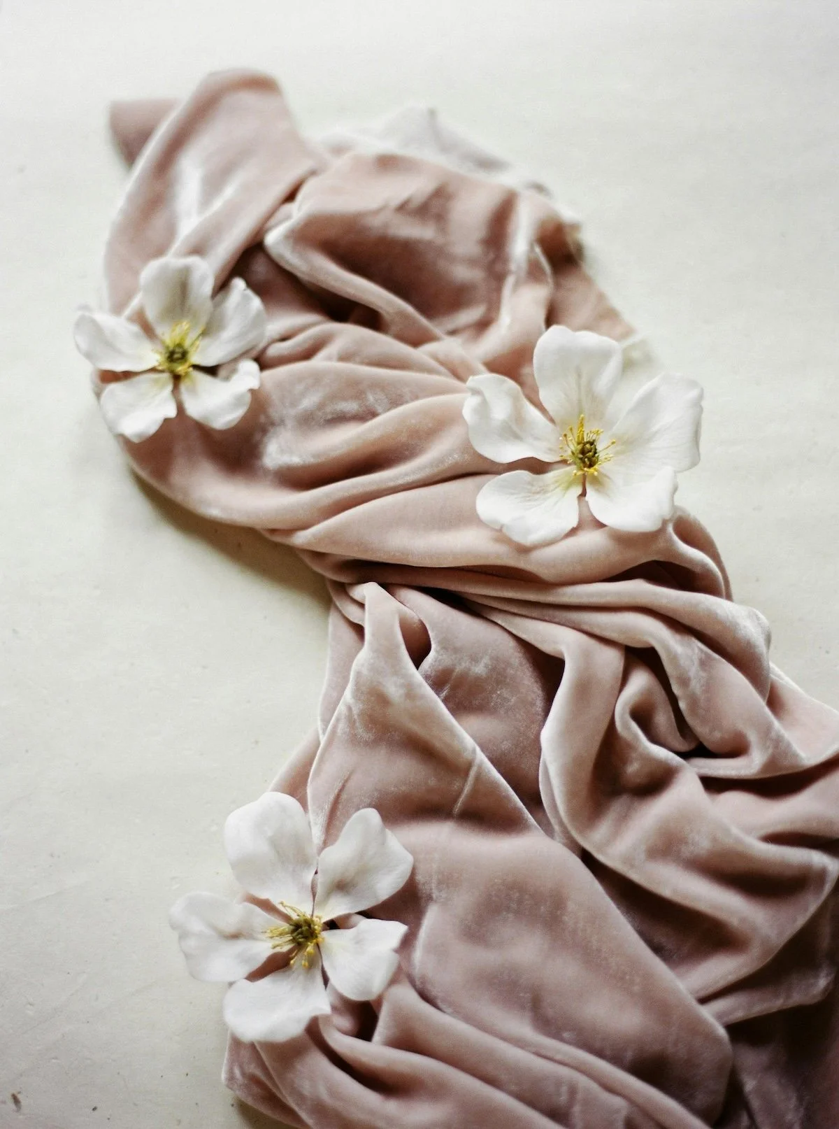 A soft pink velvet scrunchie decorated with white flowers with yellow centers.