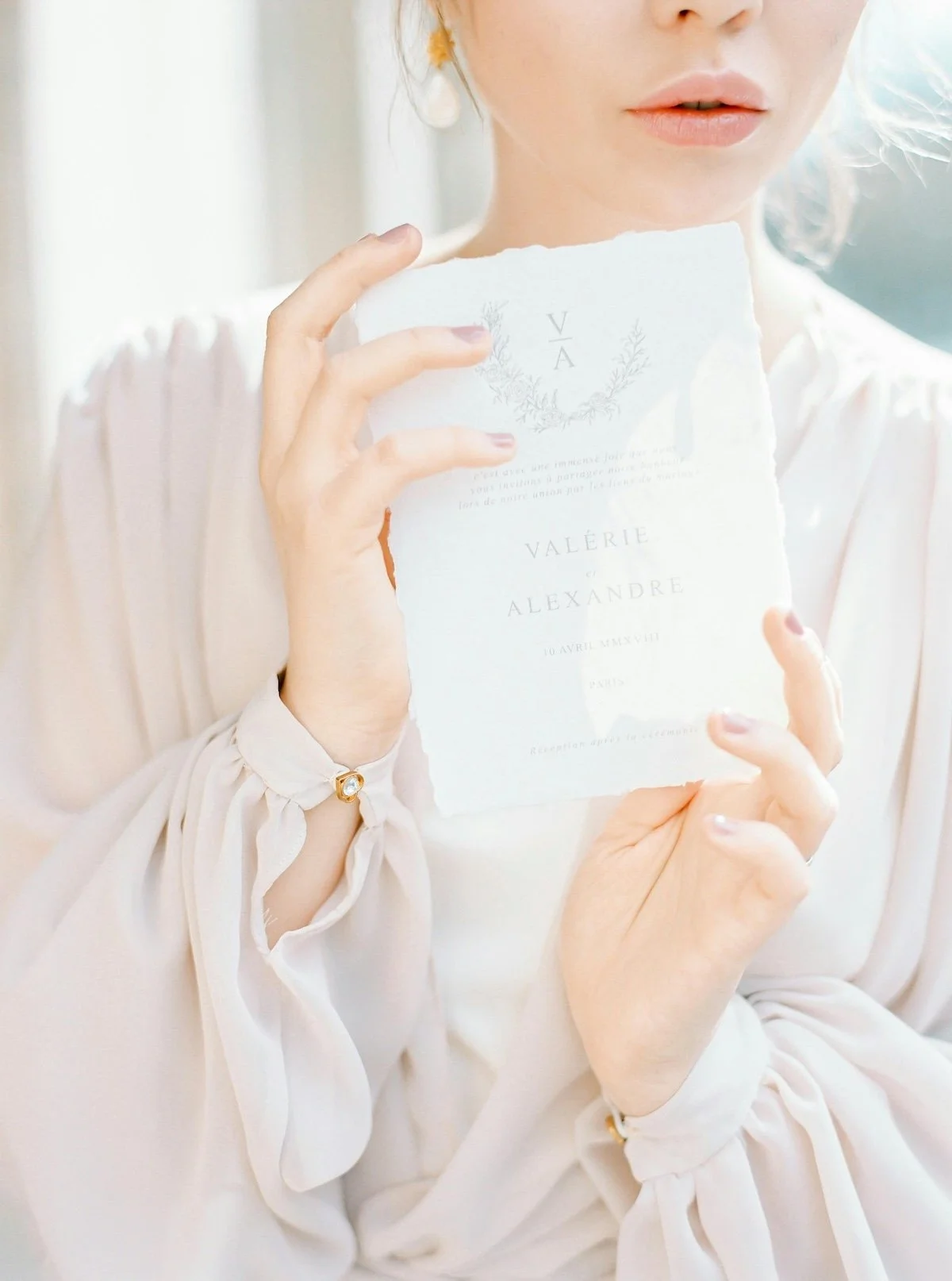 A woman in white attire holding a torn paper wedding invitation with elegant text, partially obscuring her face.