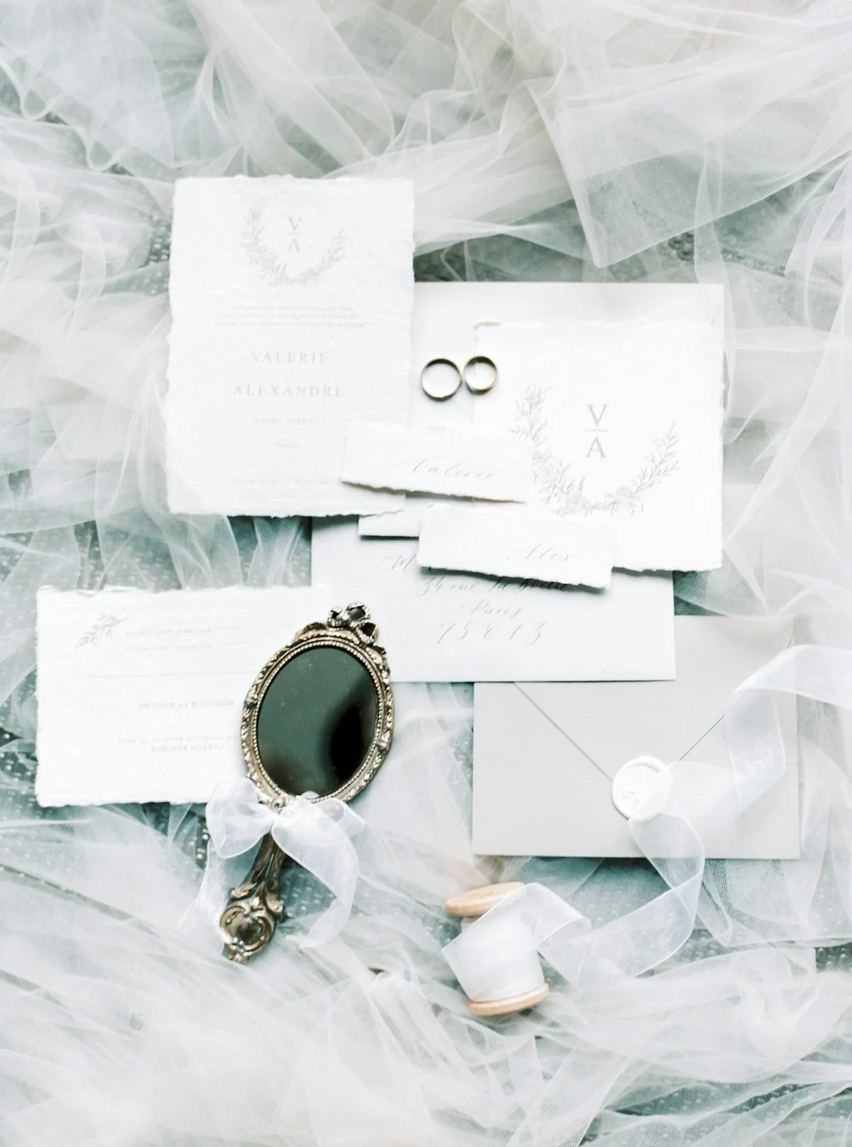 Wedding invitation suite with rings, mirror, and wedding accessories on white fabric with tulle.