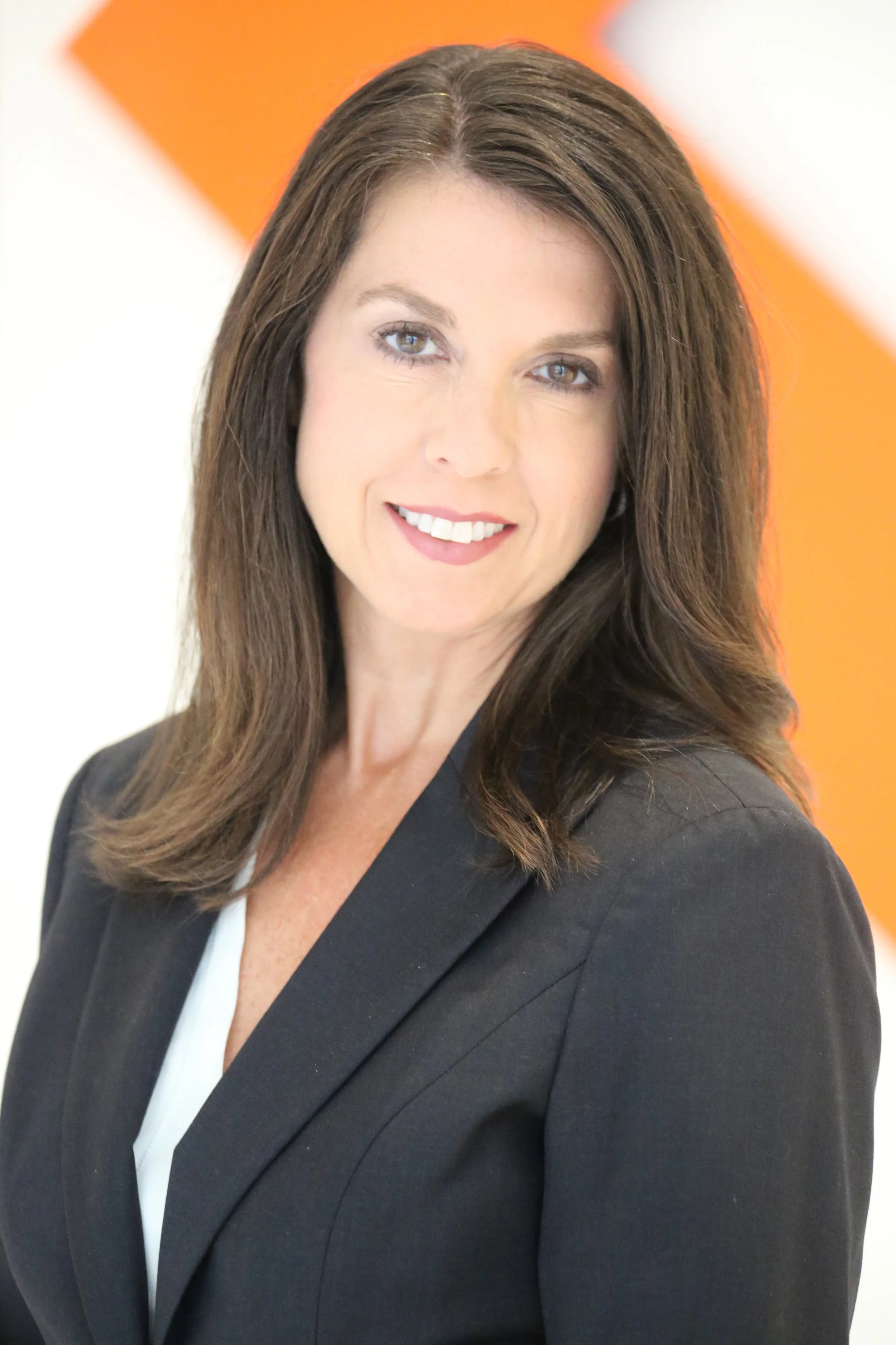 A man with wavy dark hair, light facial hair, wearing glasses and a nose ring, looking slightly to the side with a soft smile, sitting in a bright room with a blurred background and a plant.
