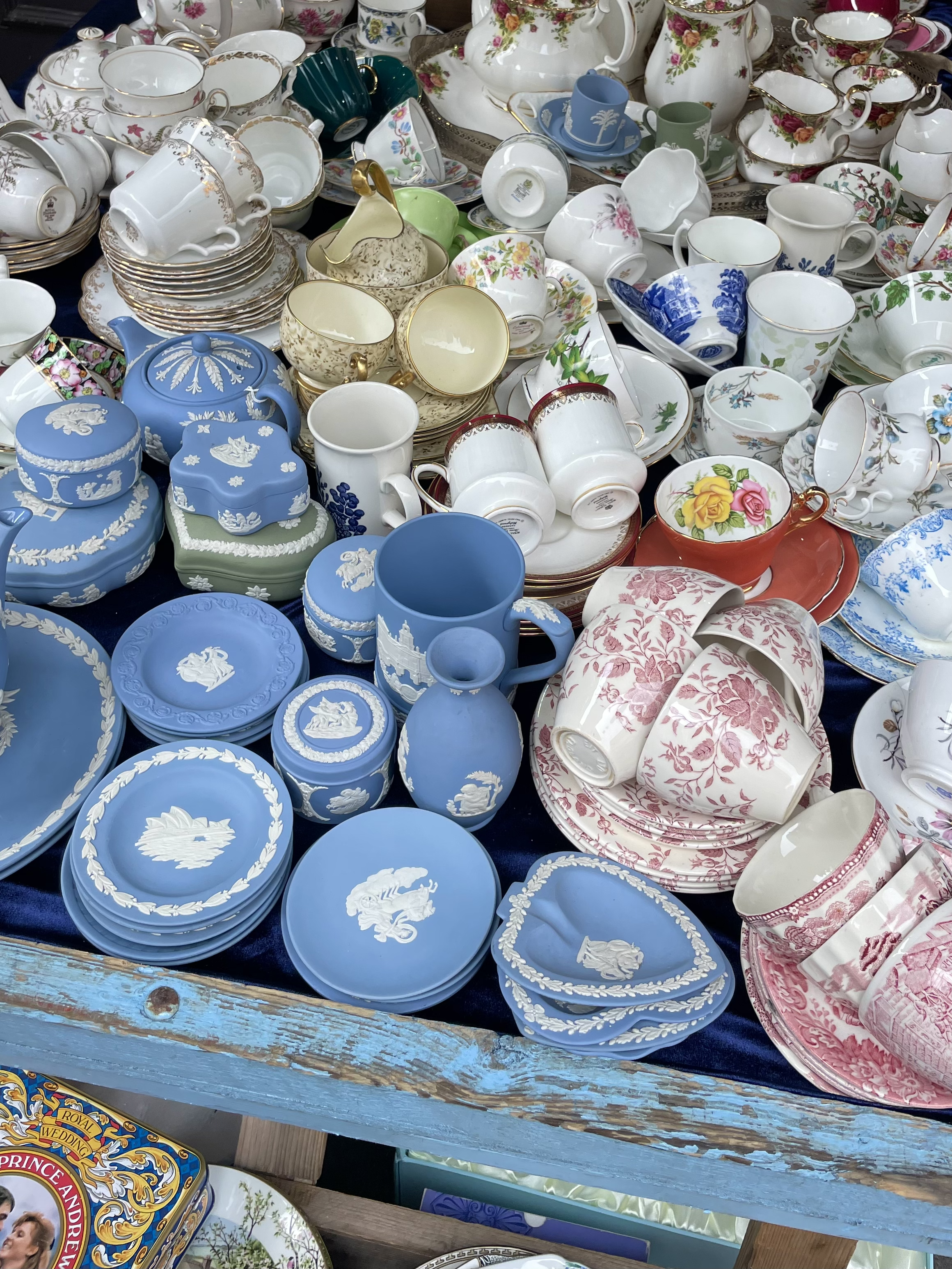 A large display of assorted fine china and porcelain dishware, including teapots, cups, saucers, plates, and decorative items in various colors like blue, white, cream, pink, and floral patterns, arranged on a wooden table in Notting Hill. 