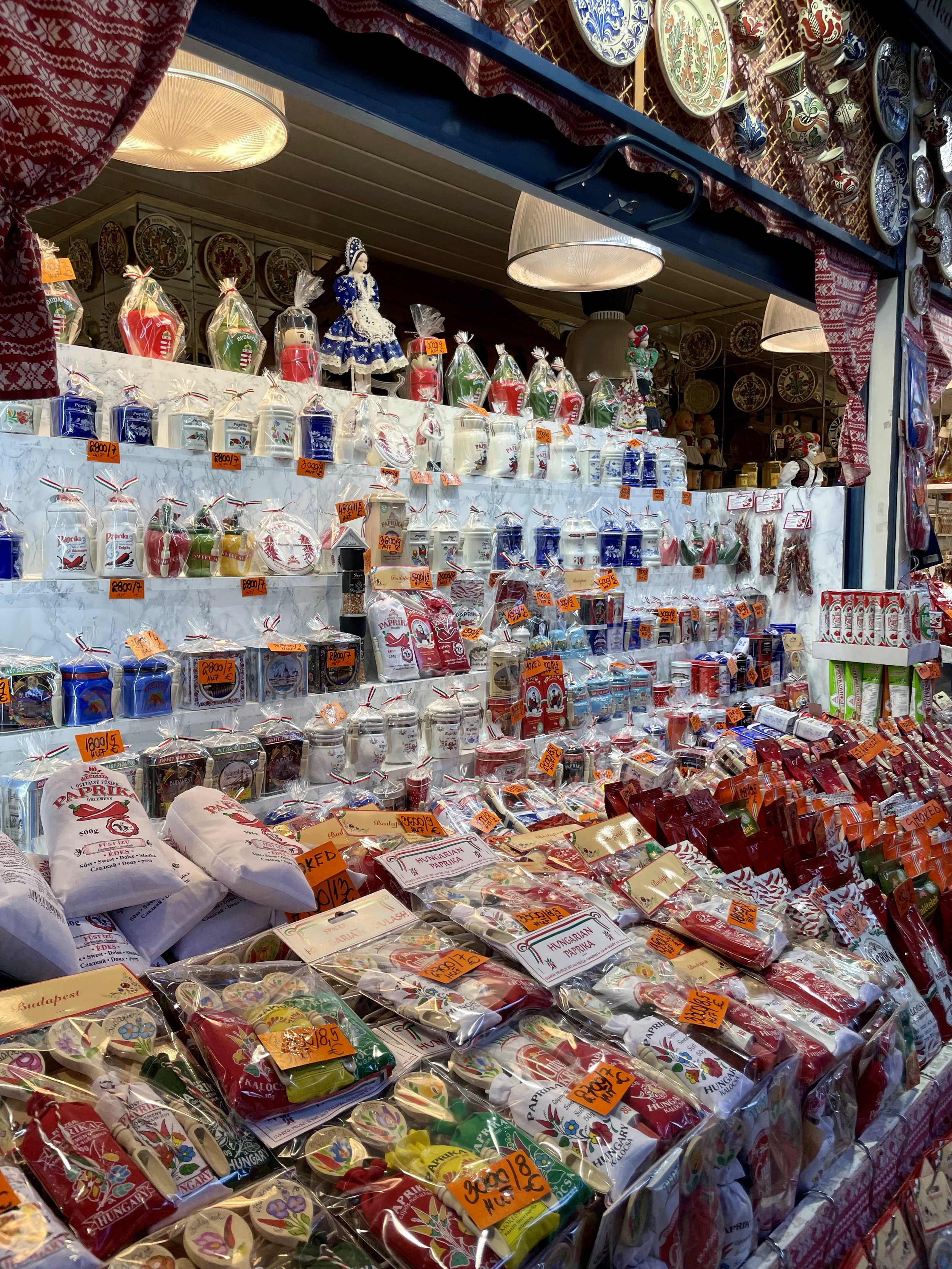 A market stall filled with Hungarian themed packaged foods, candies, and souvenirs, decorated with traditional Hungarian patterns and figurines.