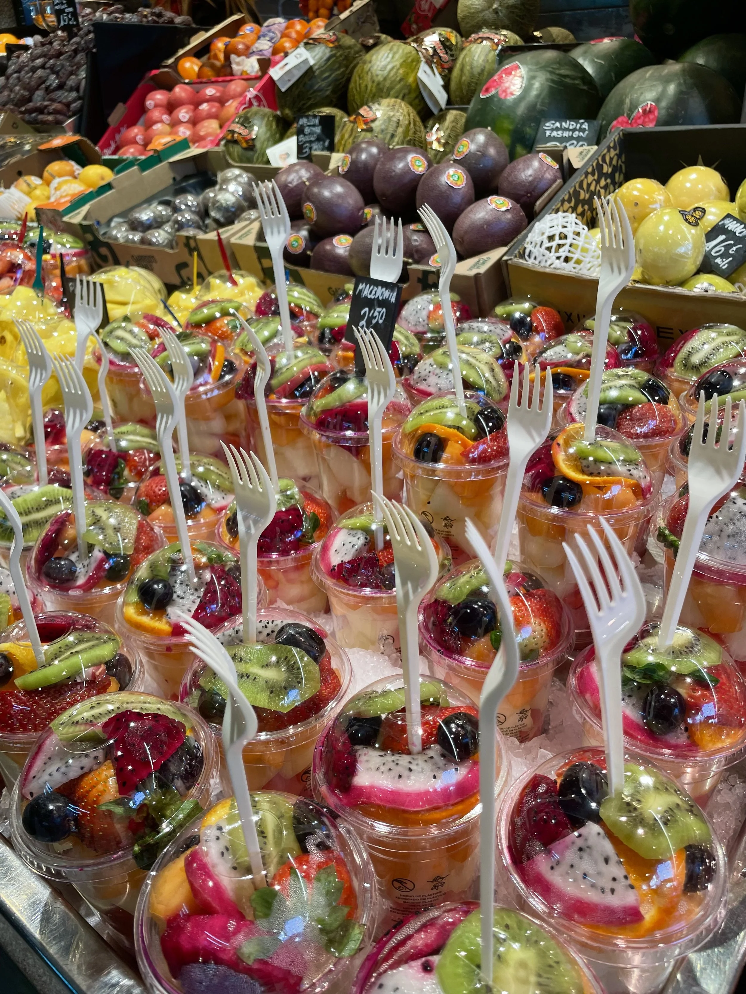 Display of pre-cut mixed fruit cups with plastic forks in a supermarket fruit section.