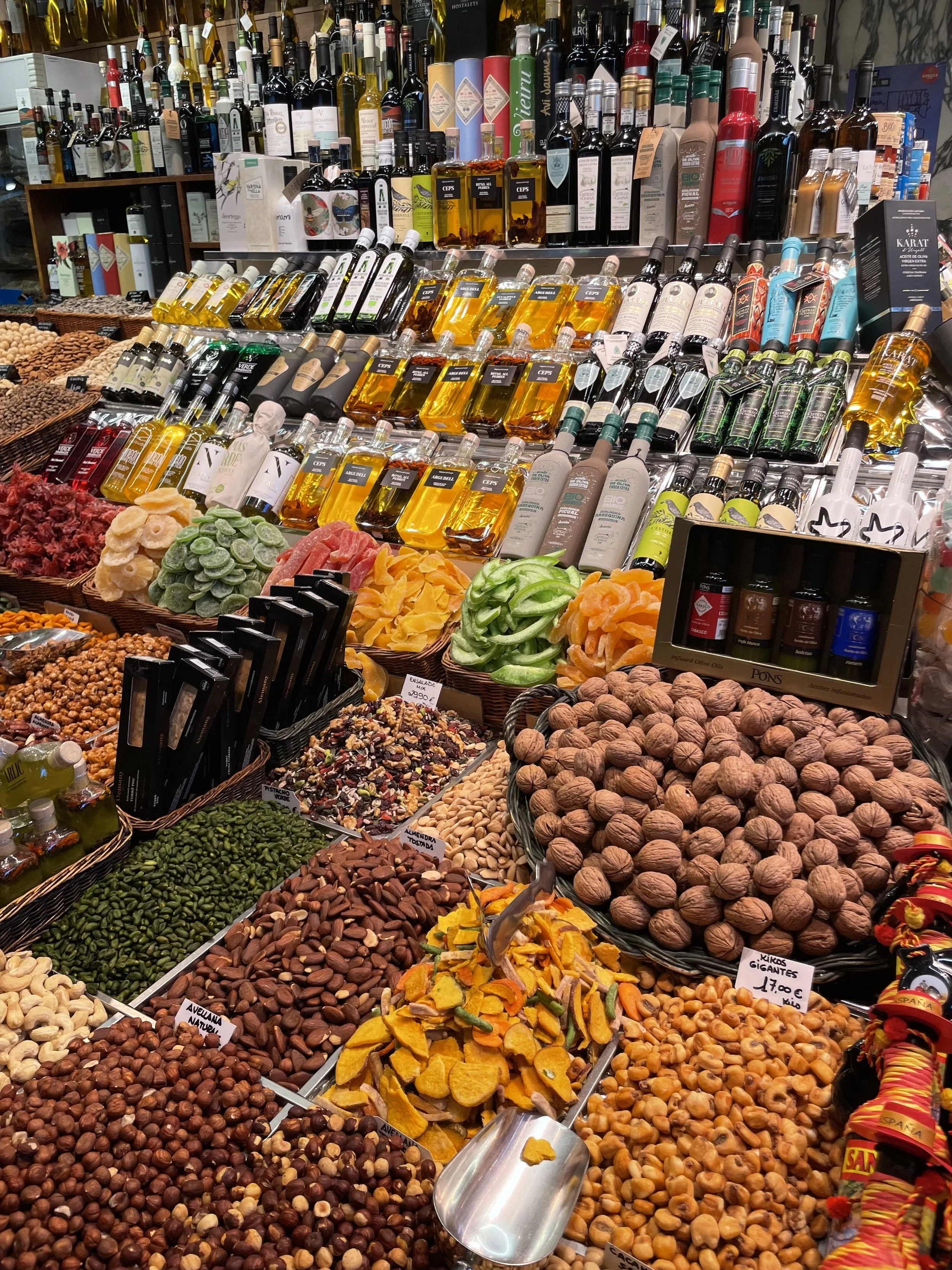 Display of various nuts, dried fruits, and bottles of oil or alcohol on shelves at a market or store.