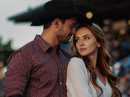 A man and woman are close together outdoors at sunset, with the man wearing a black cowboy hat and patterned shirt, and the woman with long red hair wearing a white top, looking at each other thoughtfully.
