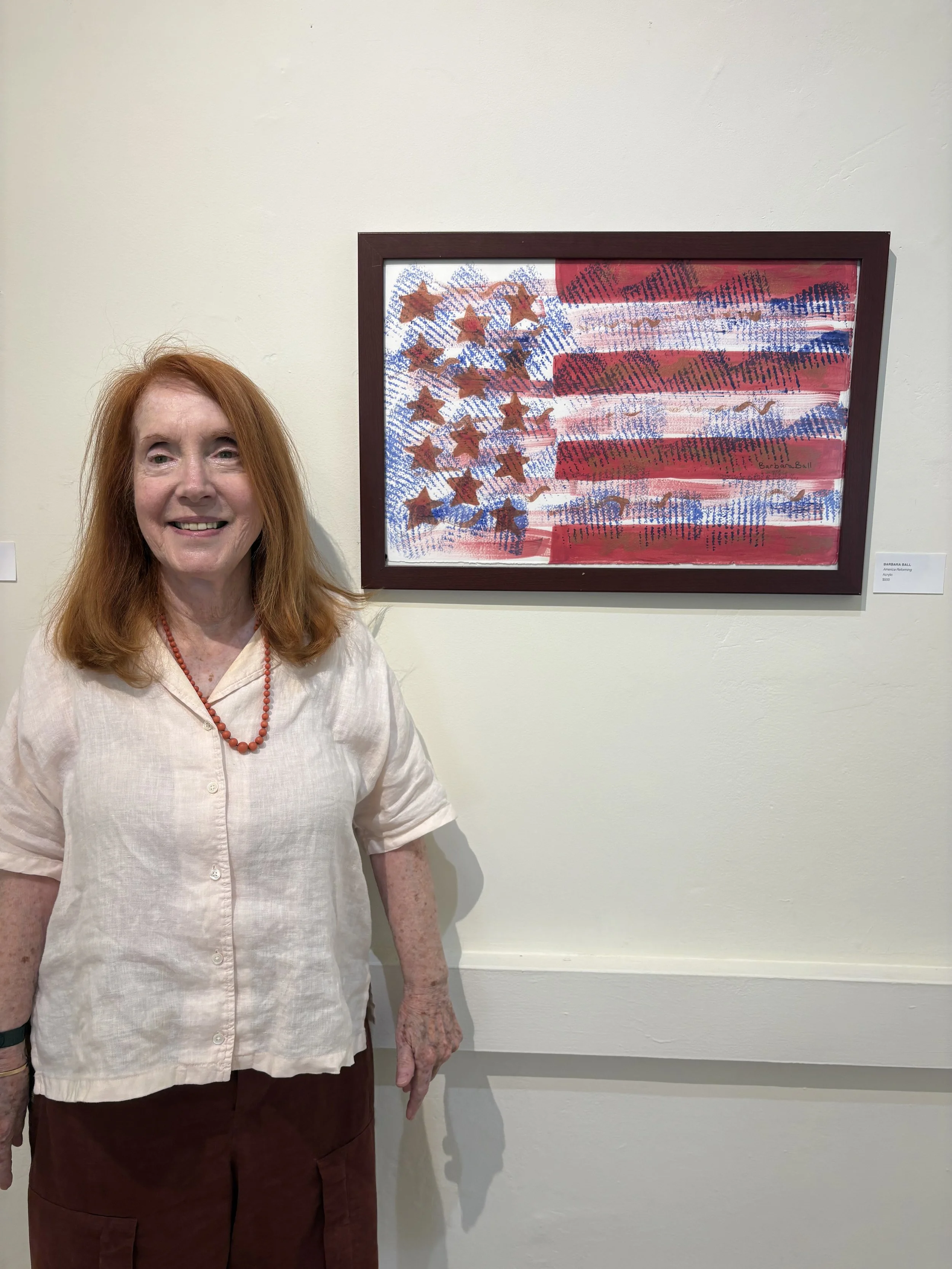 The artist Barbara Ball standing in front of one of her abstract American flag paintings