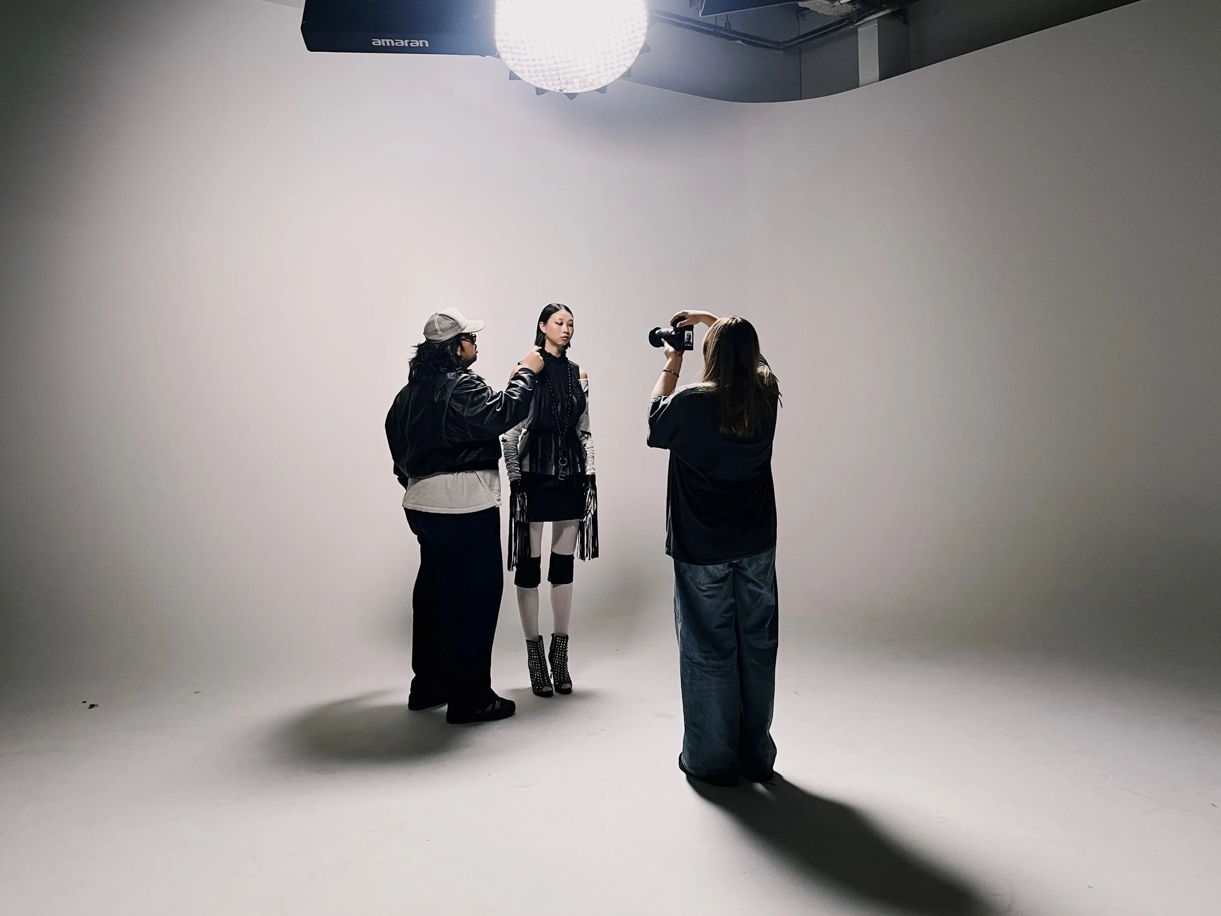 Photo of a photoshoot in a studio with a model being photographed by a photographer while assisting crew members facilitate.