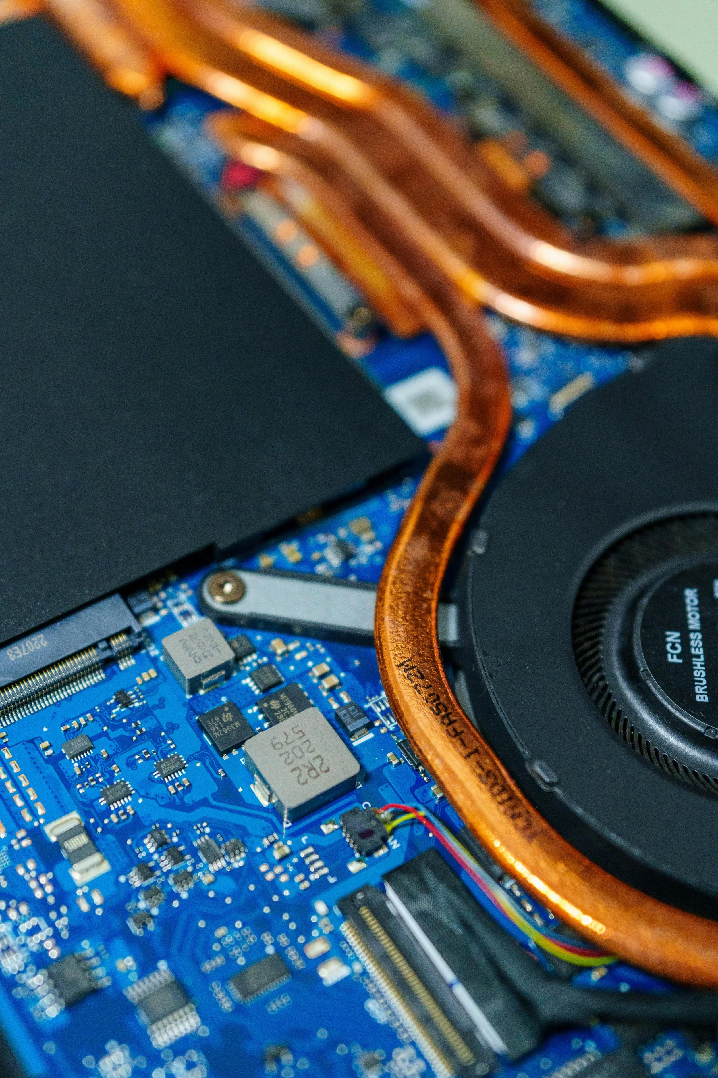 Close-up view of a computer's internal components showing a blue circuit board with electronic chips and a copper heat pipe.