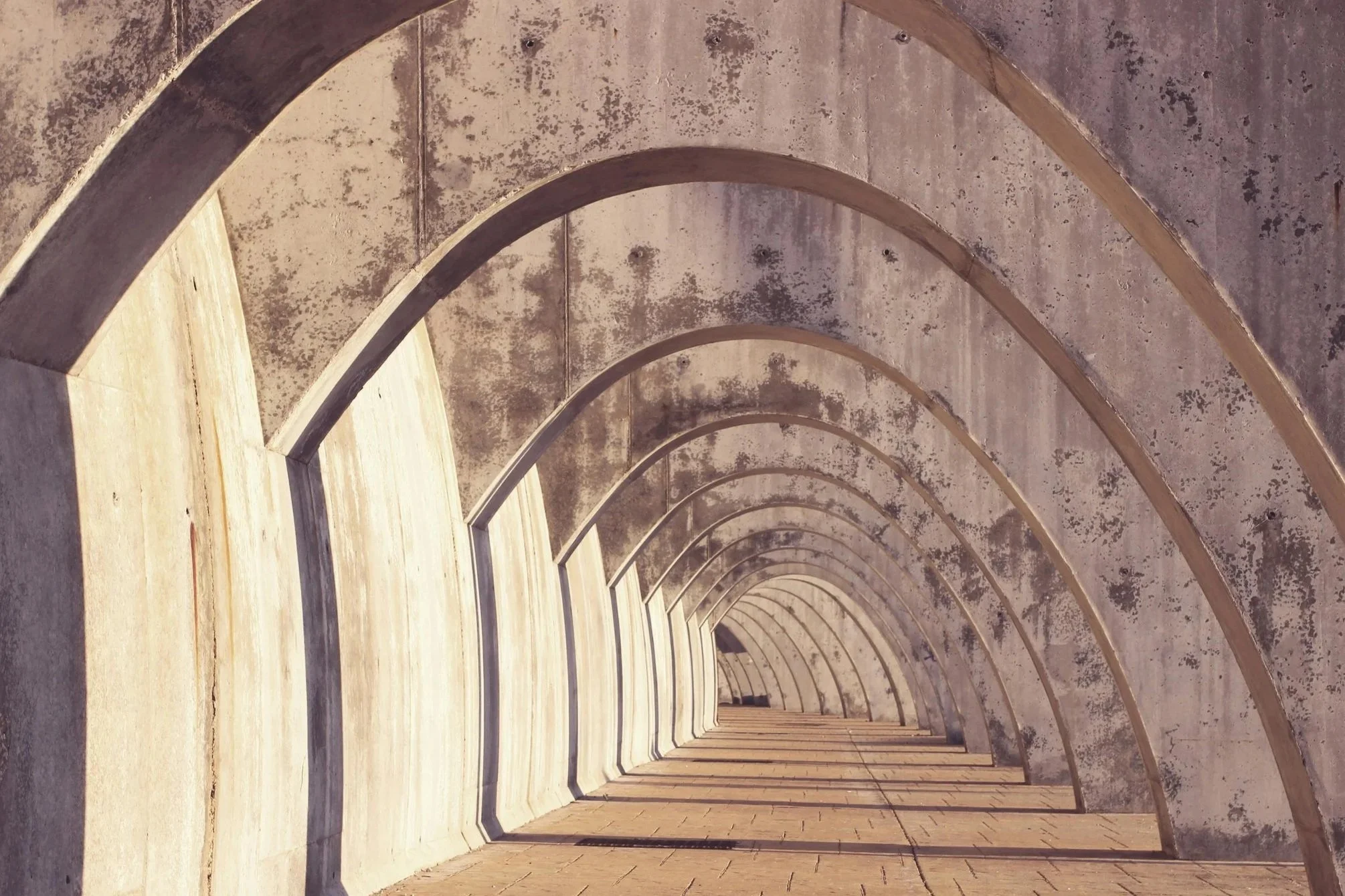 A series of concrete arches forming a tunnel with wooden floor panels.