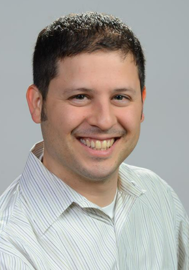Daniel B. Heyman - a smiling man with short dark hair, wearing a light-colored striped shirt, against a plain gray background.