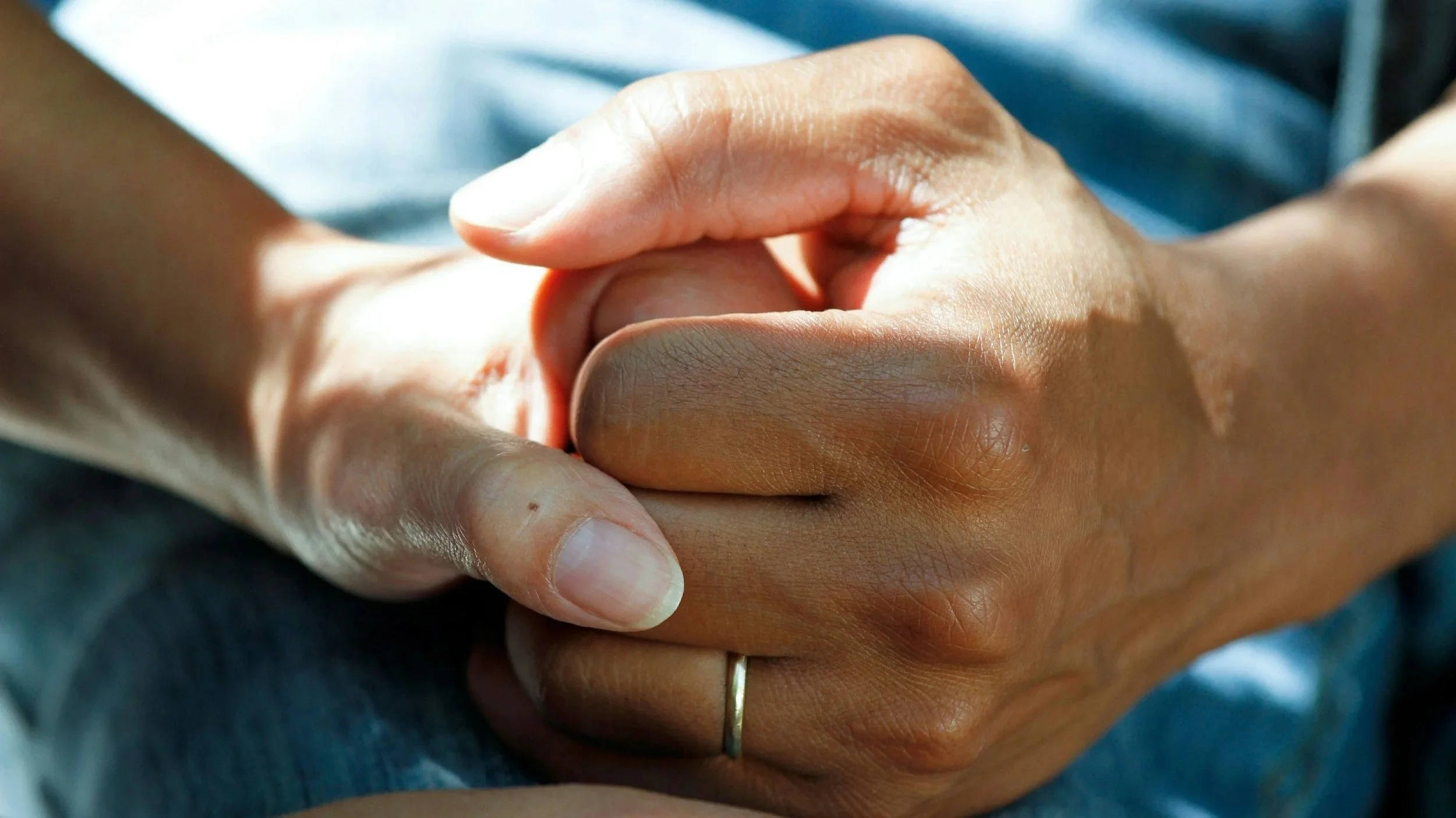 A close up of a man and woman holding hands. The image is just of the hands, set in a way that represents care.