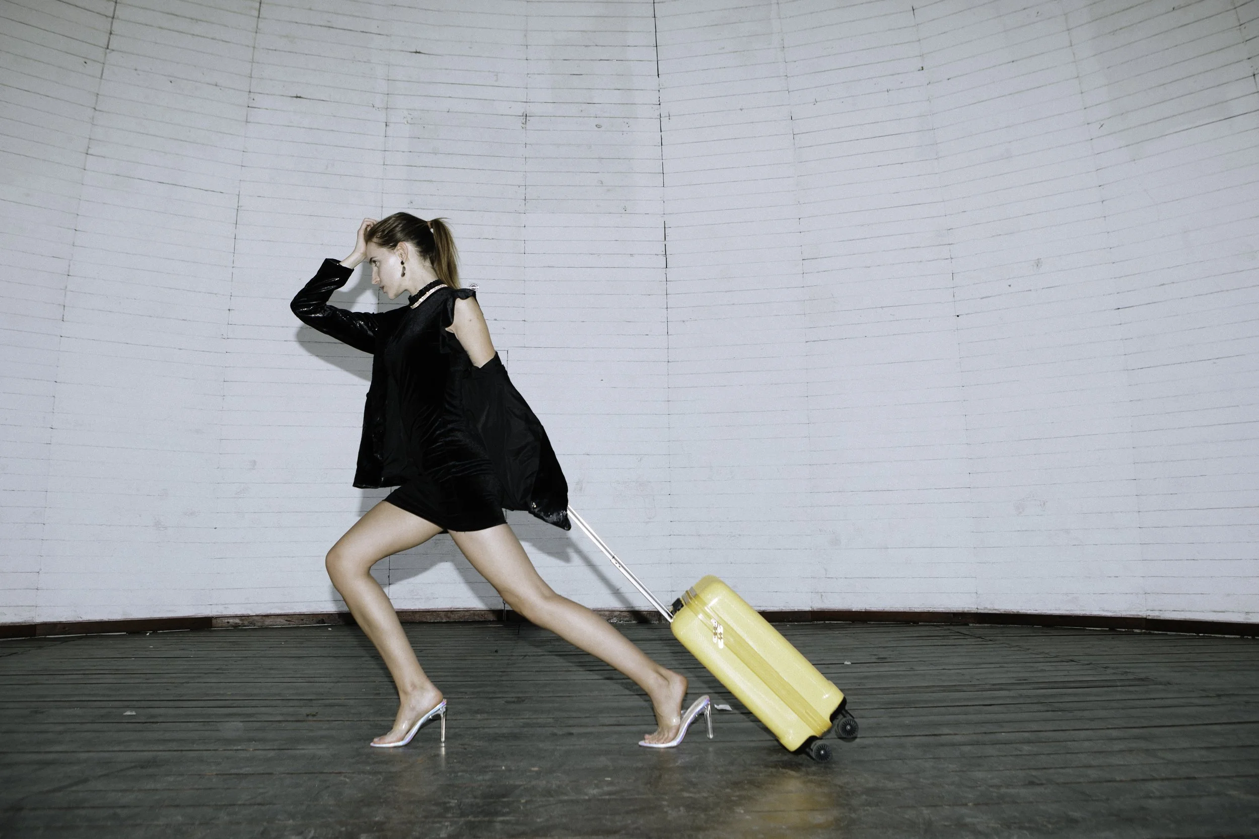A woman in high heels pulling a yellow suitcase.