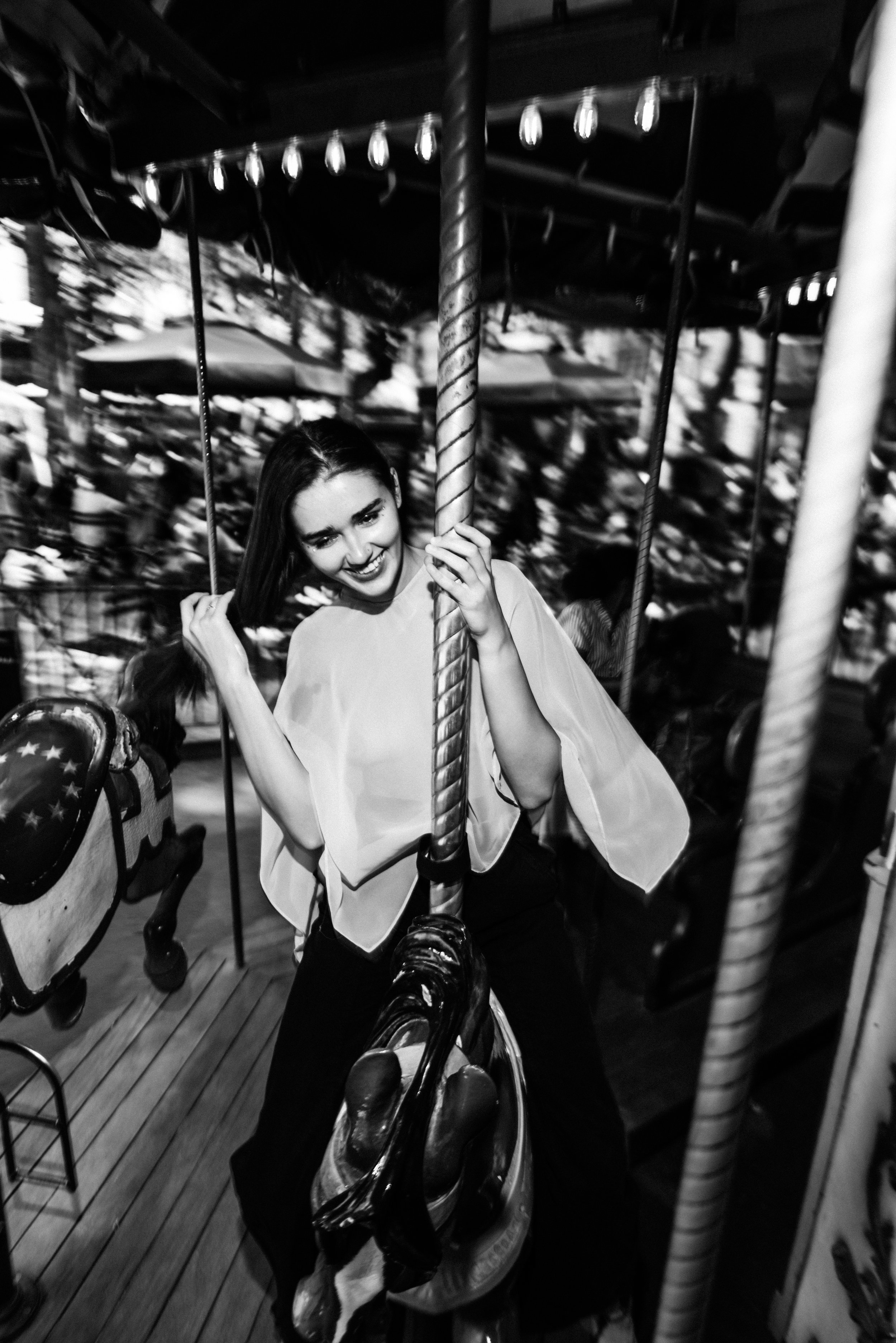 Young woman smiling and holding onto a carousel ride pole in an amusement park at night.
