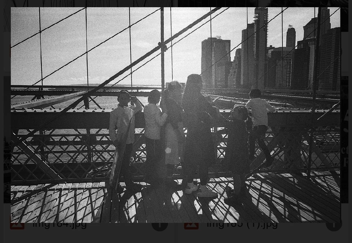 Silhouettes of people on a bridge with city skyline in the background, black and white photo.