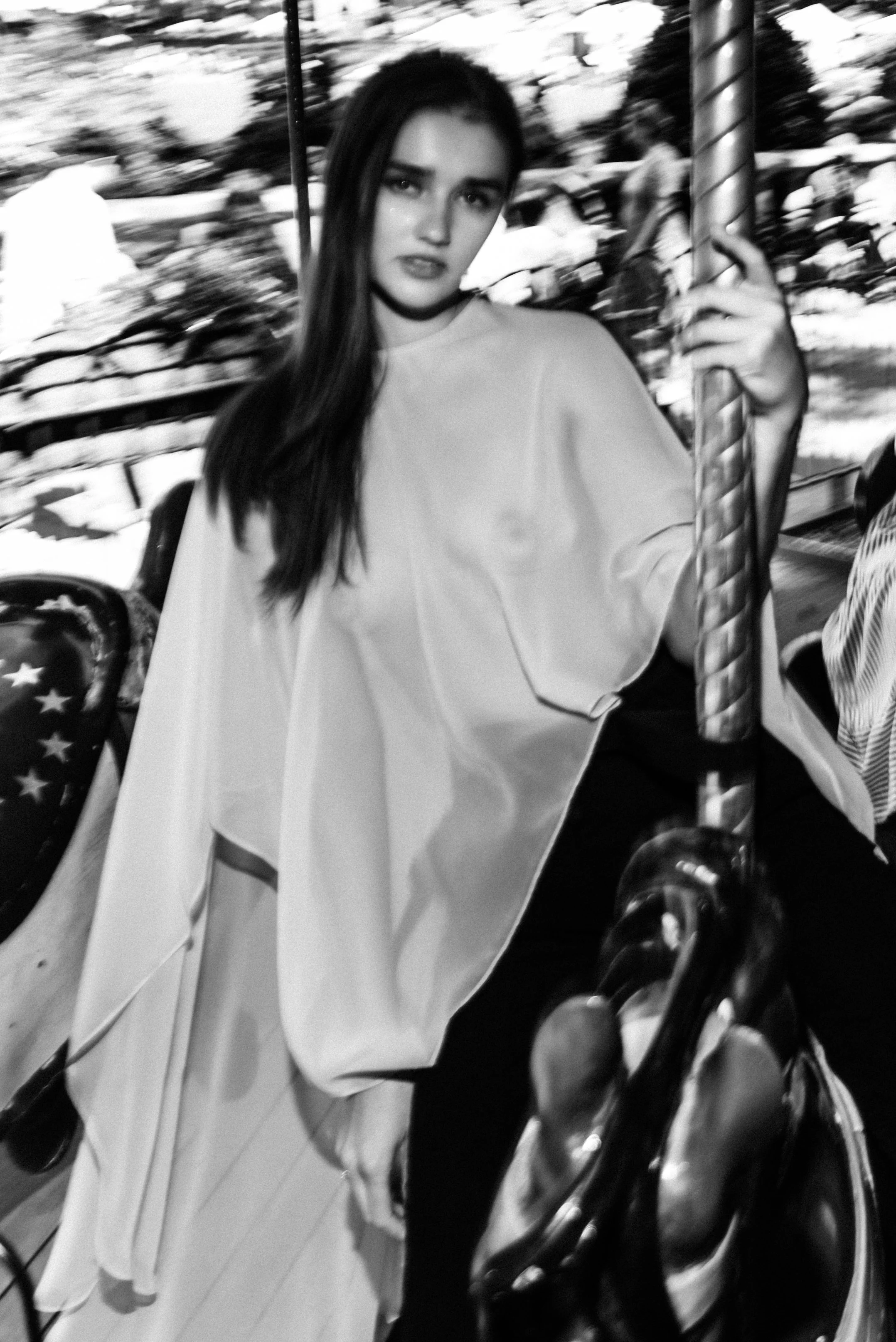 Woman with long dark hair sitting on a carousel horse, holding the pole, at an outdoor amusement park.