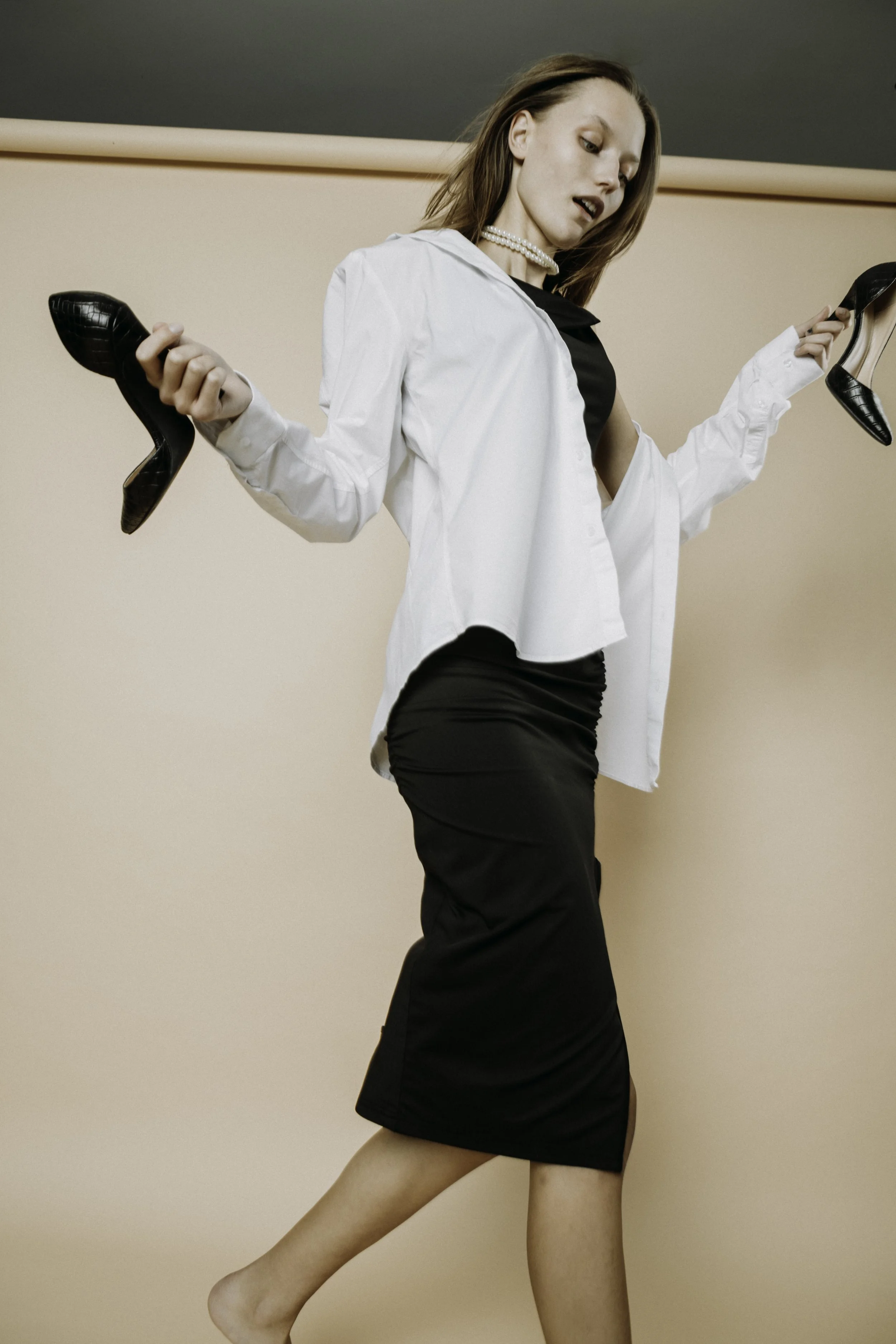 Woman in black dress and white shirt holding two black high heels