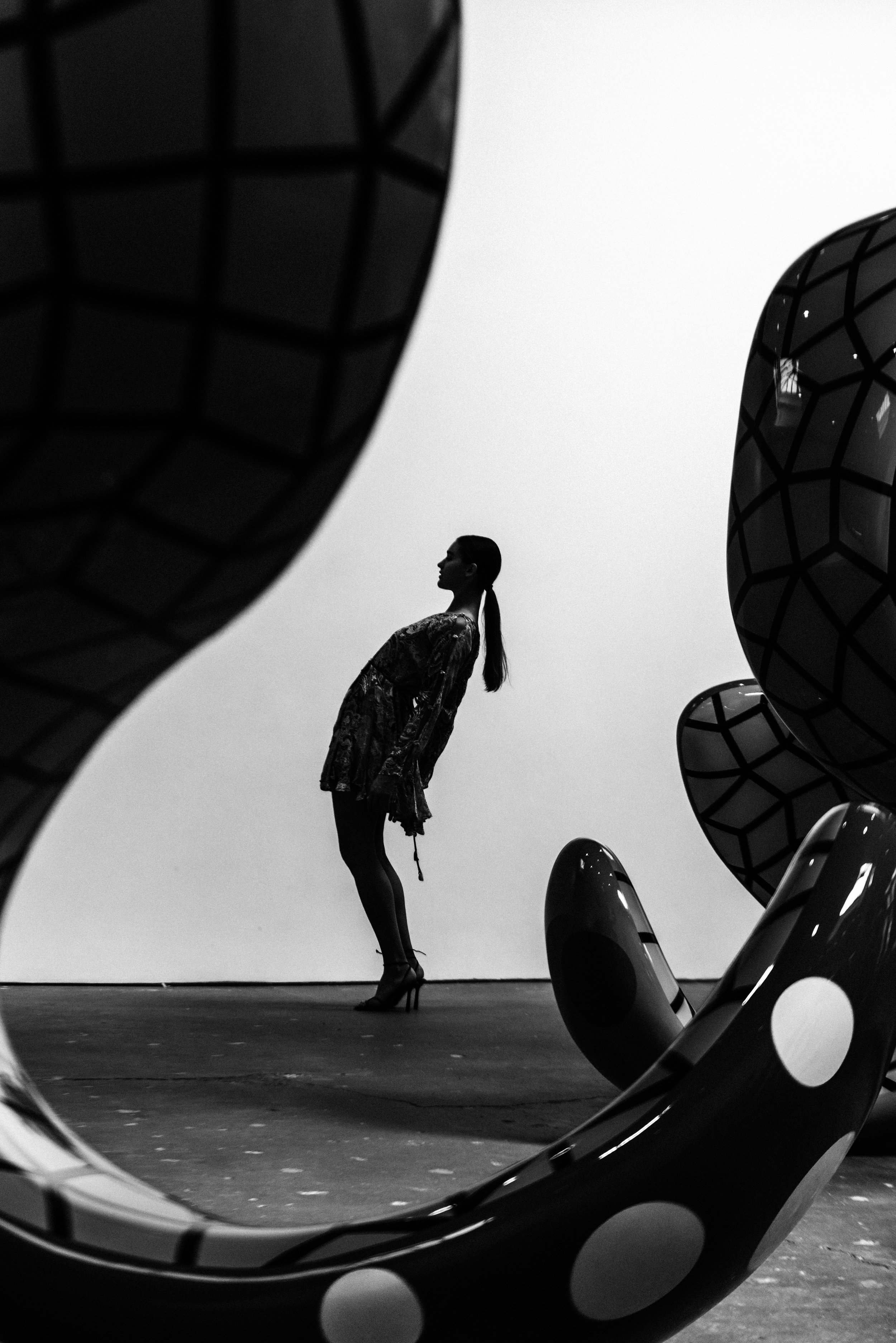 A woman posing in high heels seen through a circular sculpture with black and white dotted pattern, black and white photo.