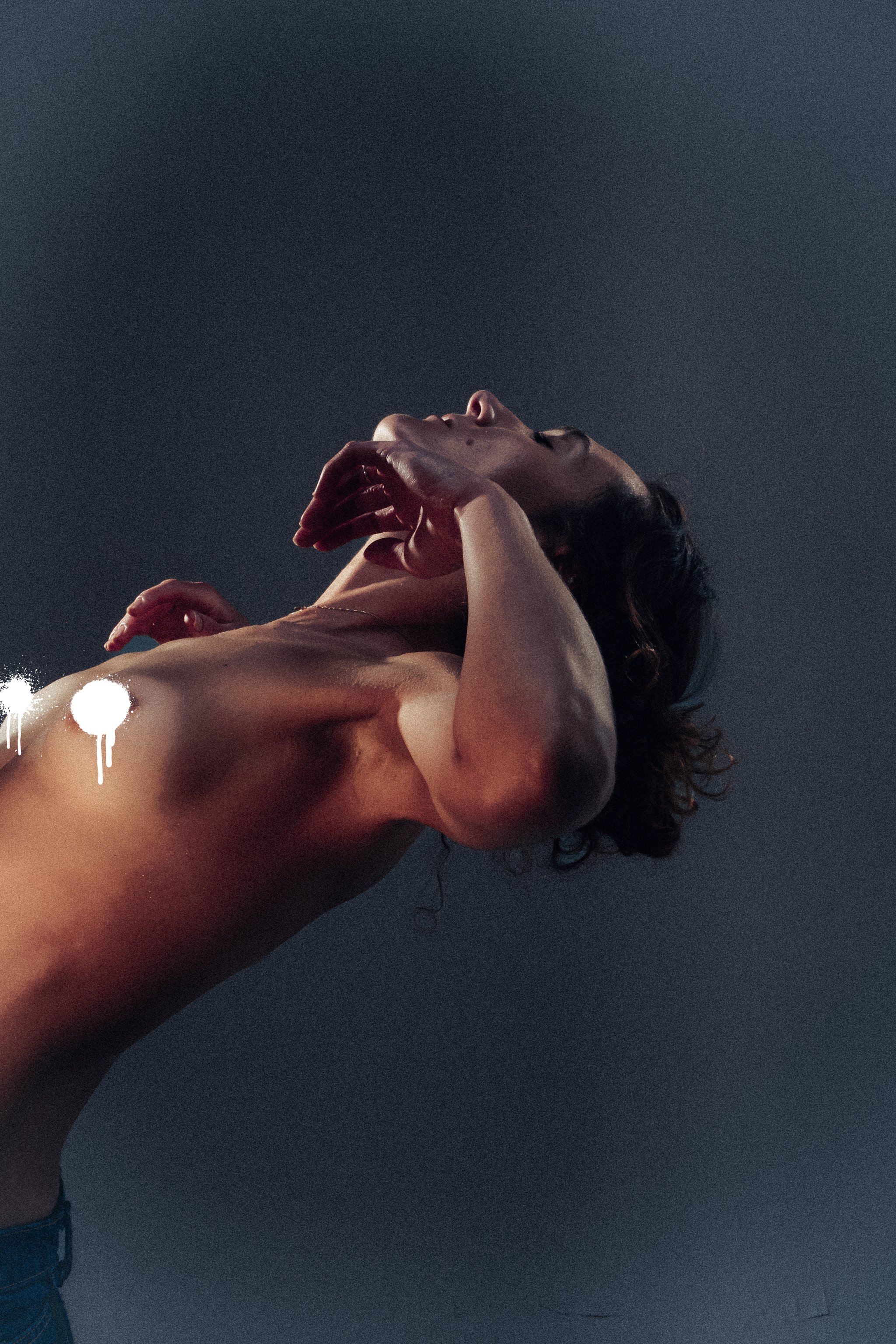 A woman with shoulder-length hair posing against a dark background, with one hand on her face and her head tilted back.