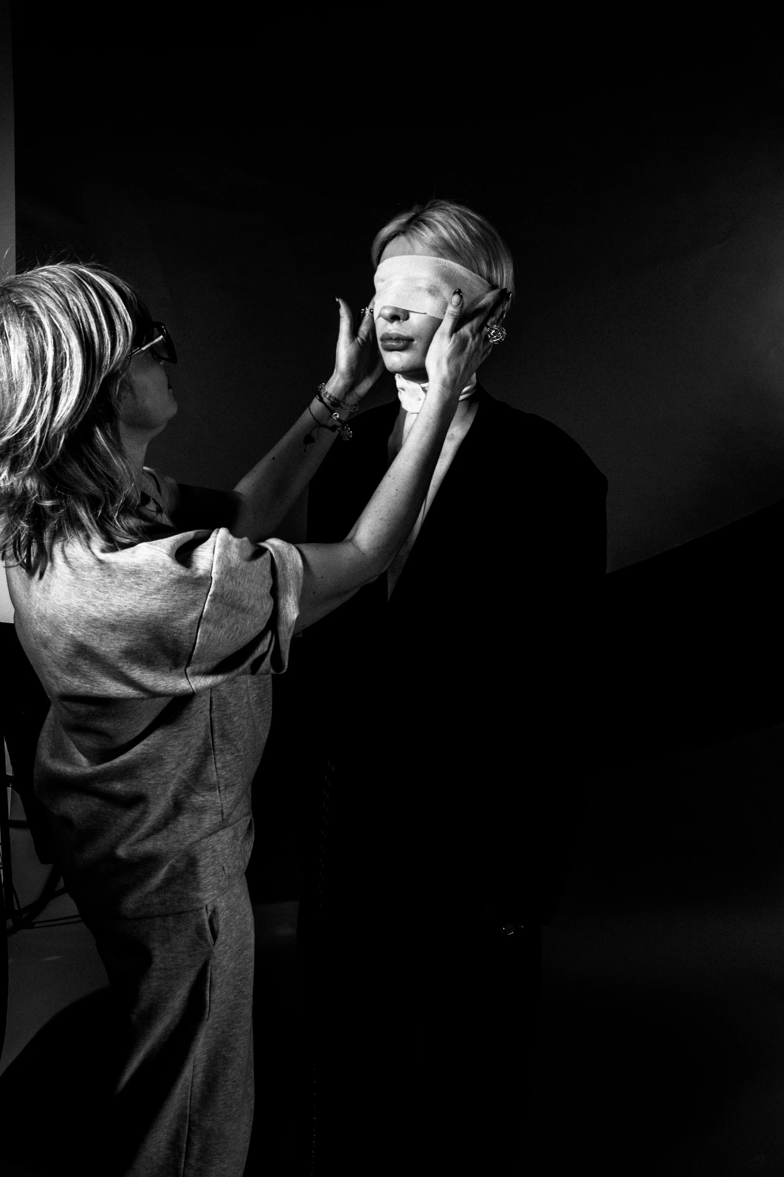 Lady adjusting a model's blindfold during a photoshoot in black and white.