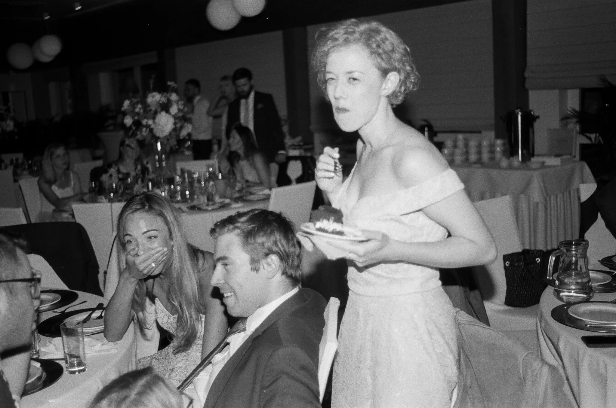 A woman in a wedding dress holding a plate with cake, serving guests at a wedding reception.