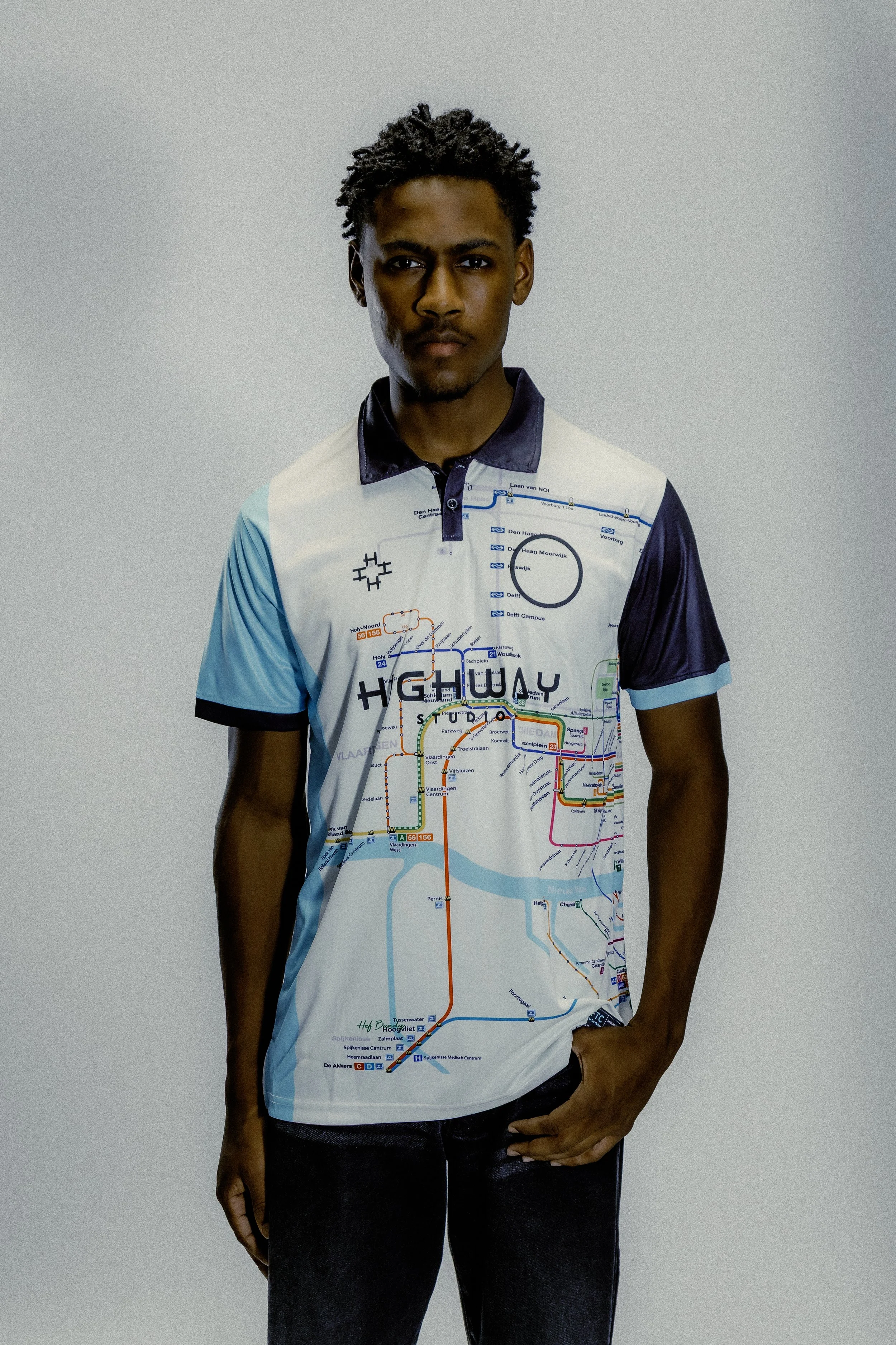 A young man wearing a collared shirt with a transit map design on it, standing against a plain background.