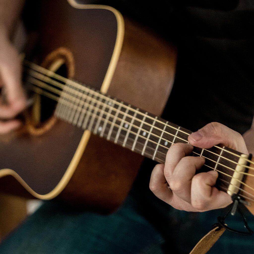 Person playing an acoustic guitar with a focus on the fretboard and hand positioning.
