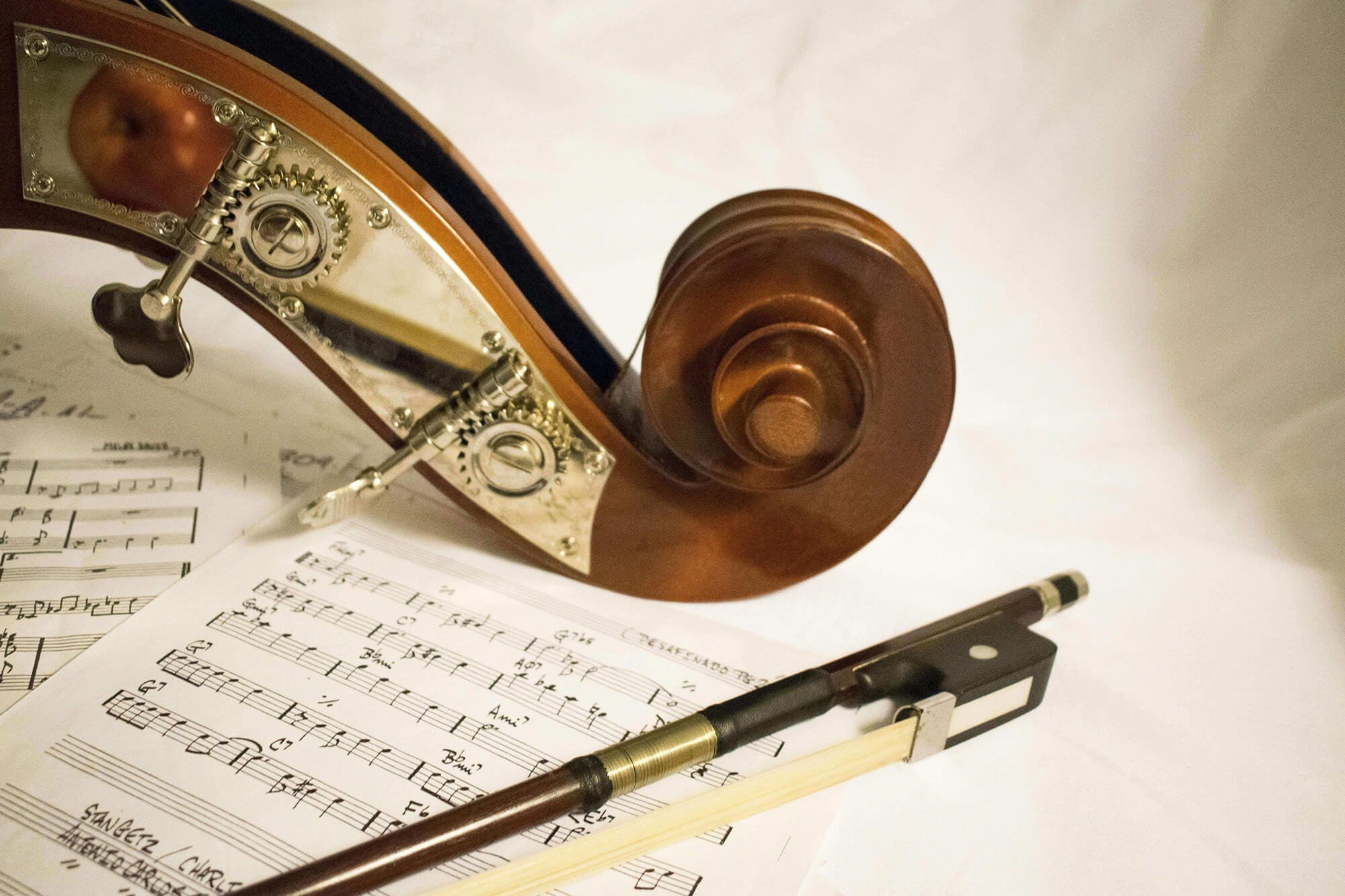 Close-up of a sheet of printed music surrounded by pens and a wooden clock, with part of a violin visible in the background.