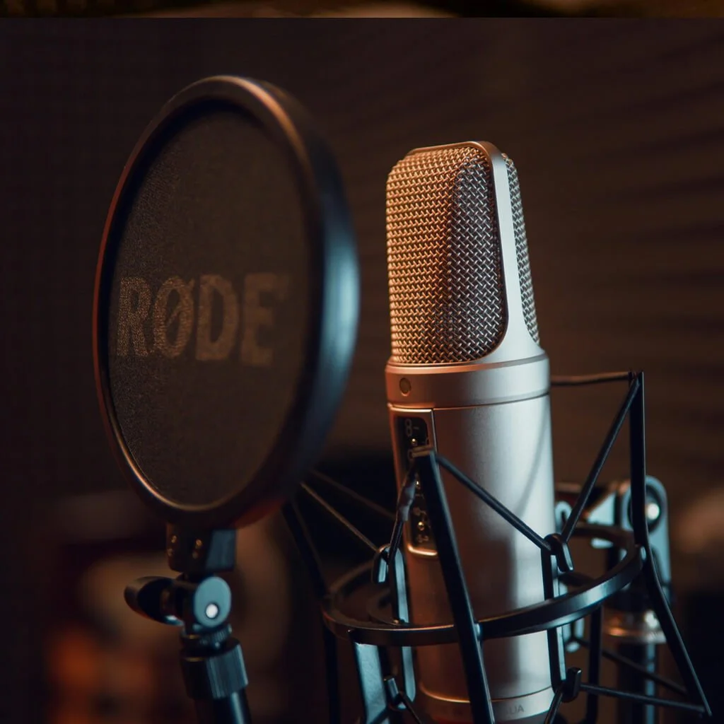 A professional studio microphone with a pop filter in front of it, set against a dark background.