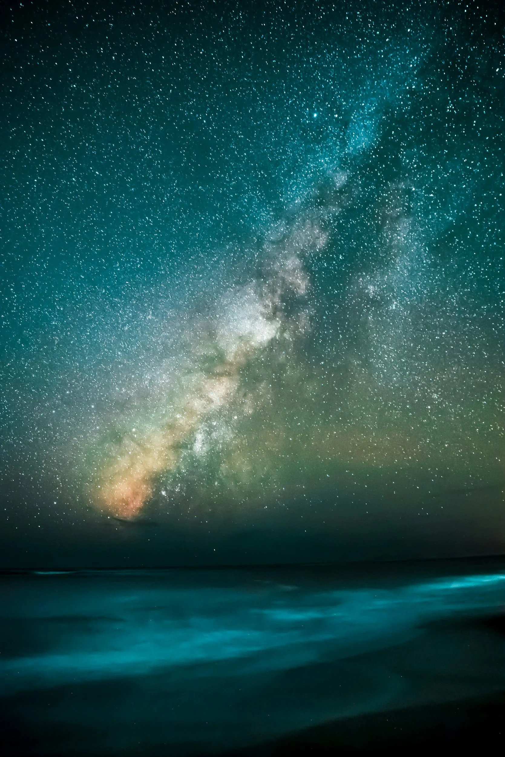 Night sky filled with stars and the Milky Way galaxy over a calm ocean with gentle waves reminding us of past life regression hypnosis and our soul journeys.
