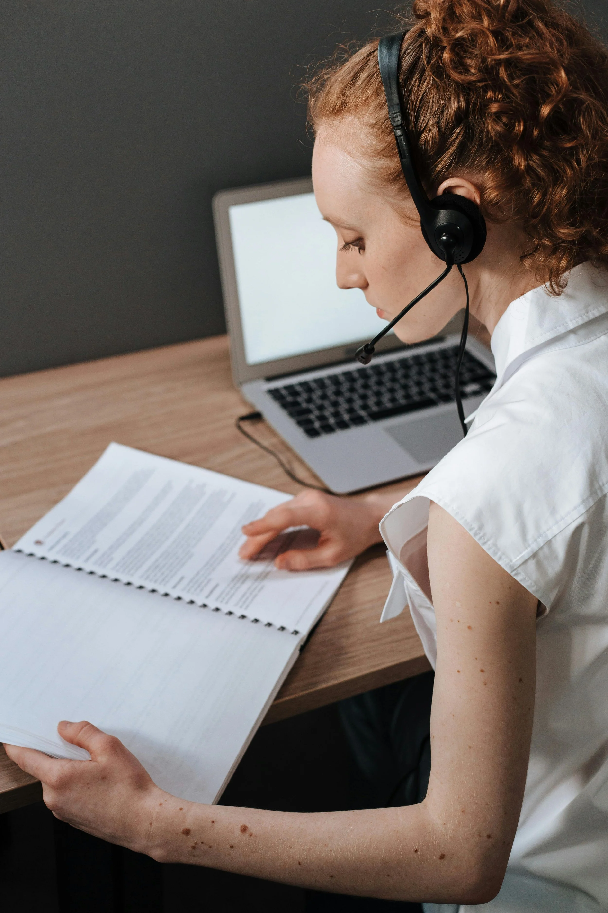 A woman sitting at a desk looking at a training manual possibly taking online hypnotherapy certification training