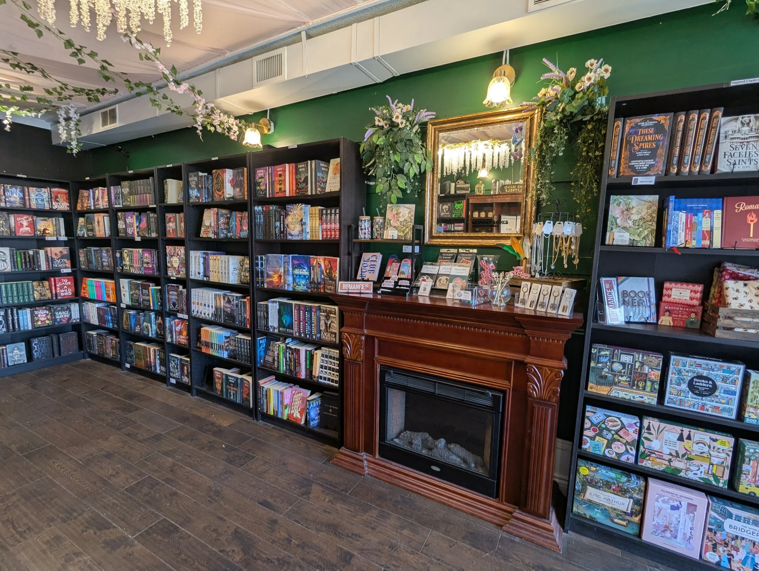 A bookstore with shelves filled with books, a wooden fireplace mantle, and decorative flowers and greenery on the walls.