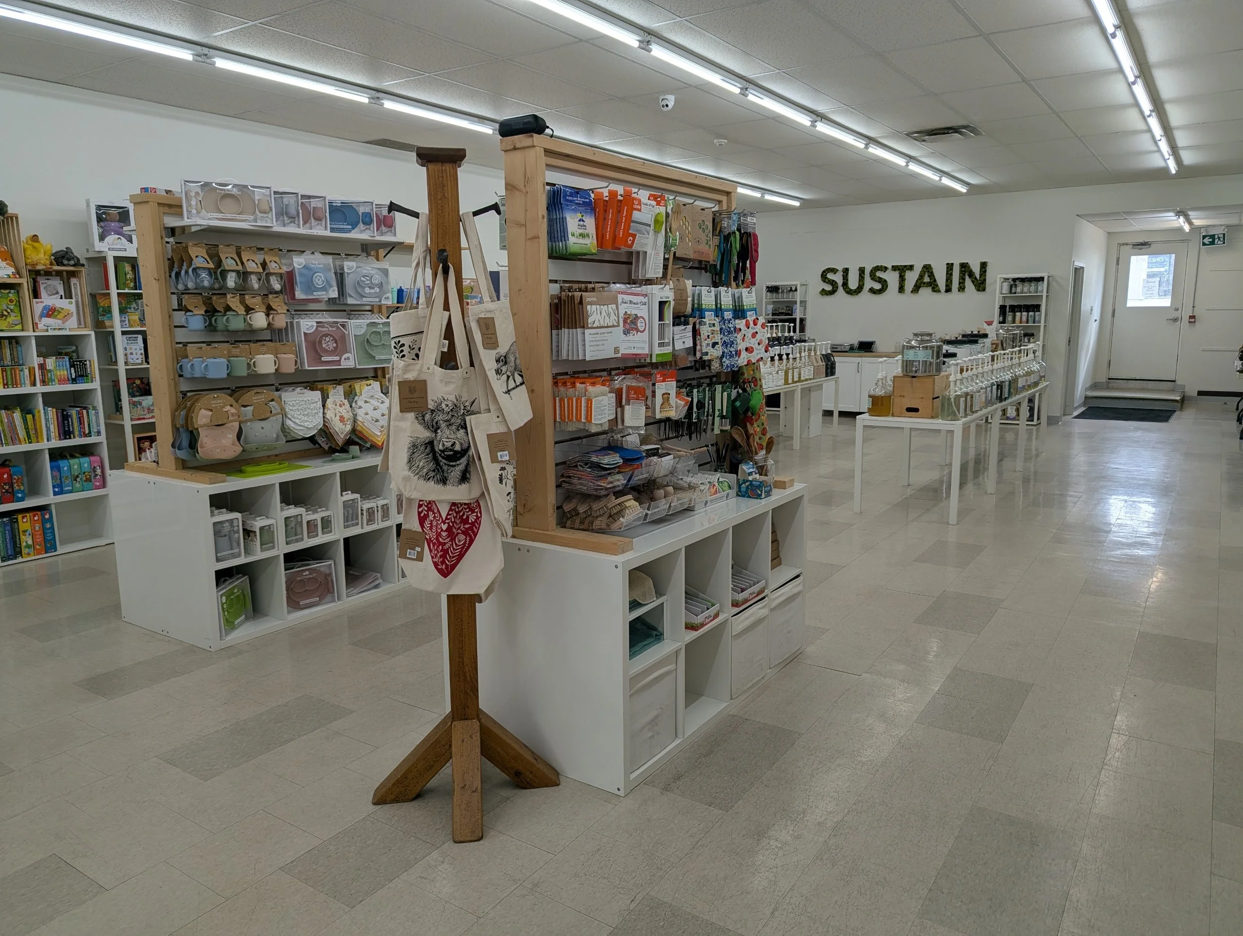 Interior of a retail store with shelves displaying various household and kitchen products. The store has a sign on the wall that reads "SUSTAIN."