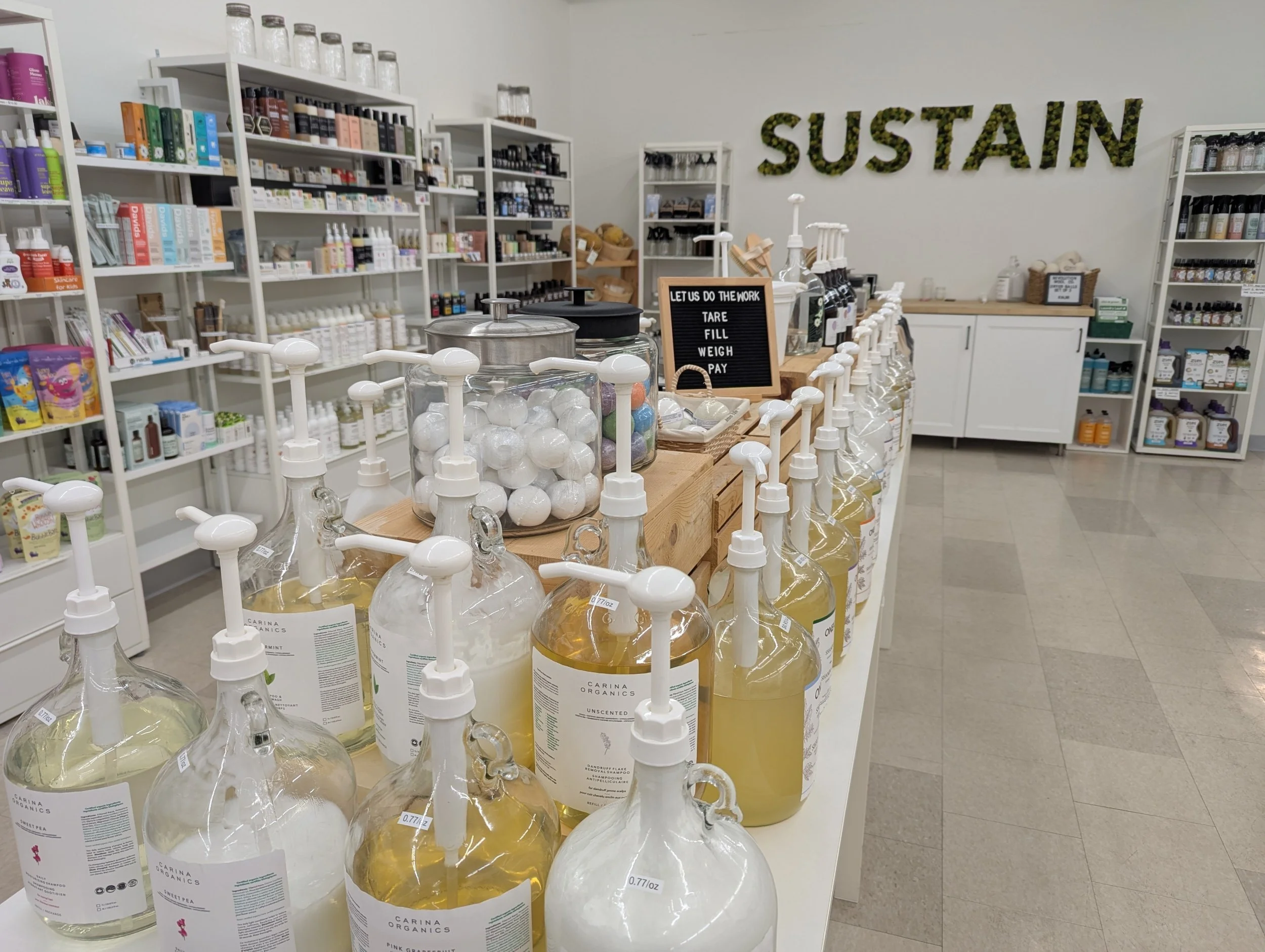 A store interior with shelves stocked with organic personal care products and bottles of liquid soap or shampoo. Large letters spelling 'SUSTAIN' are on the wall.