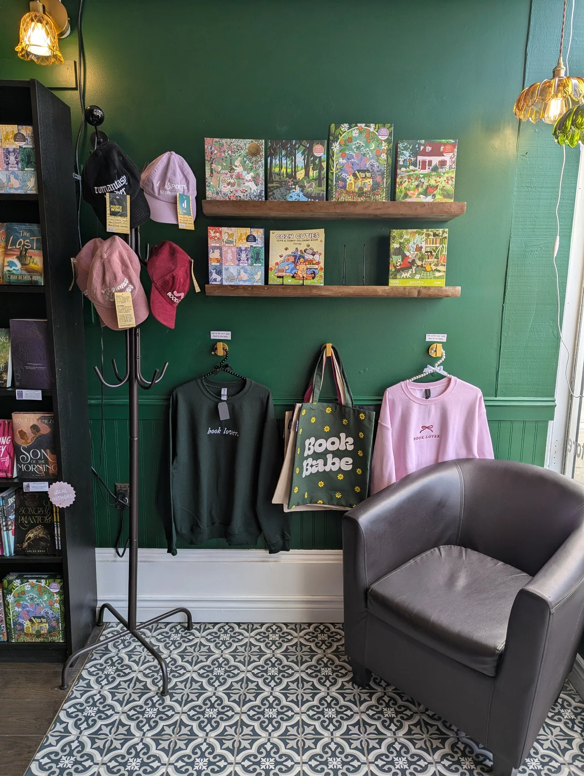 Display of children's books, hats, and clothing in a bookstore or gift shop with green walls and patterned tile floor.