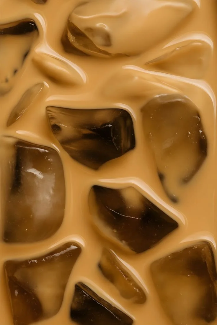 Close-up of iced coffee with ice cubes and a creamy, light brown liquid.