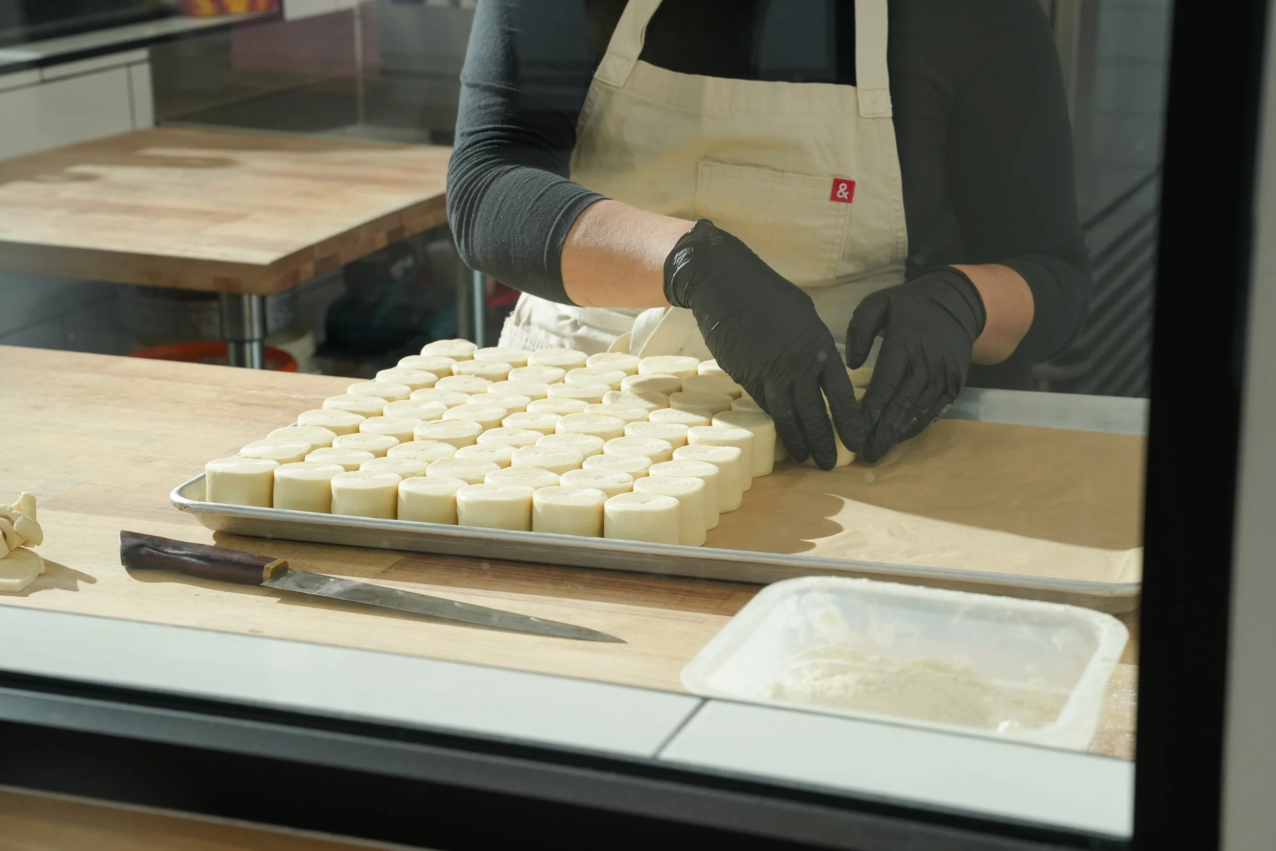 Person in black gloves and beige apron arranging round white cheese wheels on a tray in a cheese-making facility.