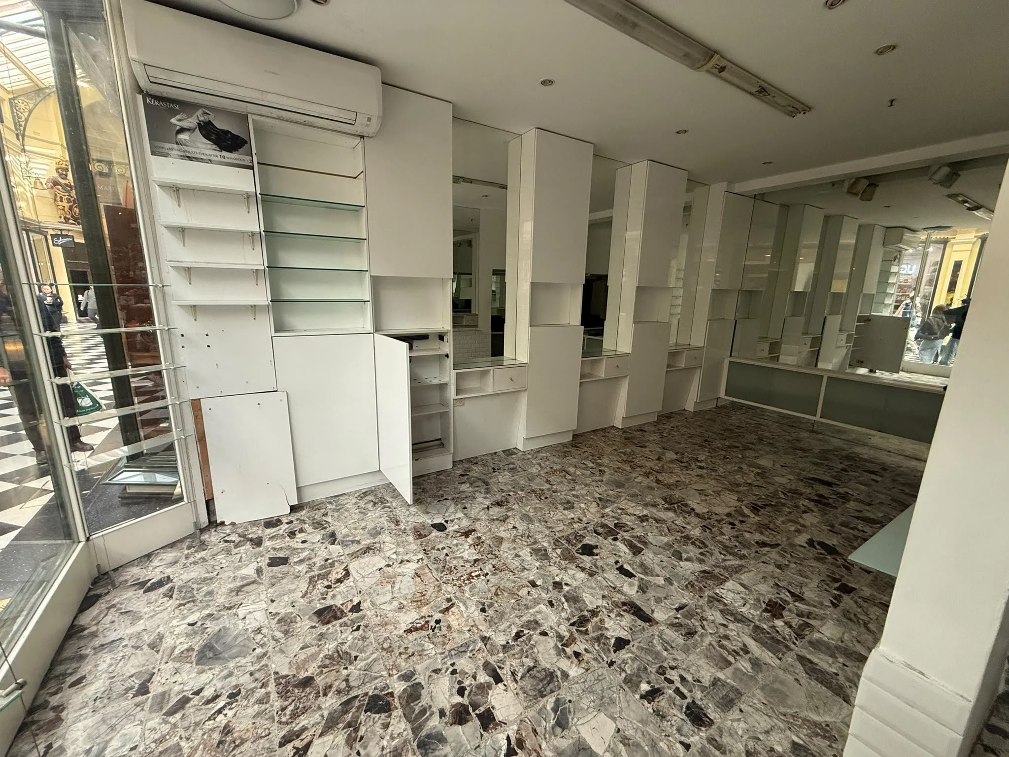 Empty retail space in Melbourne ready for demolition with white shelving units, a glass display case, and a terrazzo floor inside a shopping mall.